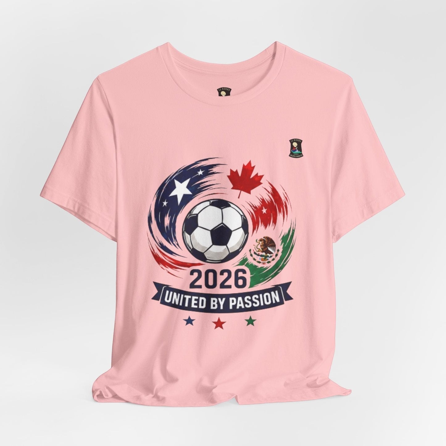 CJ Riders Foundation Store pink 100% cotton t-shirt with 2026 soccer graphic featuring a ball, USA, Canada, Mexico flags, and "United by Passion" text.
