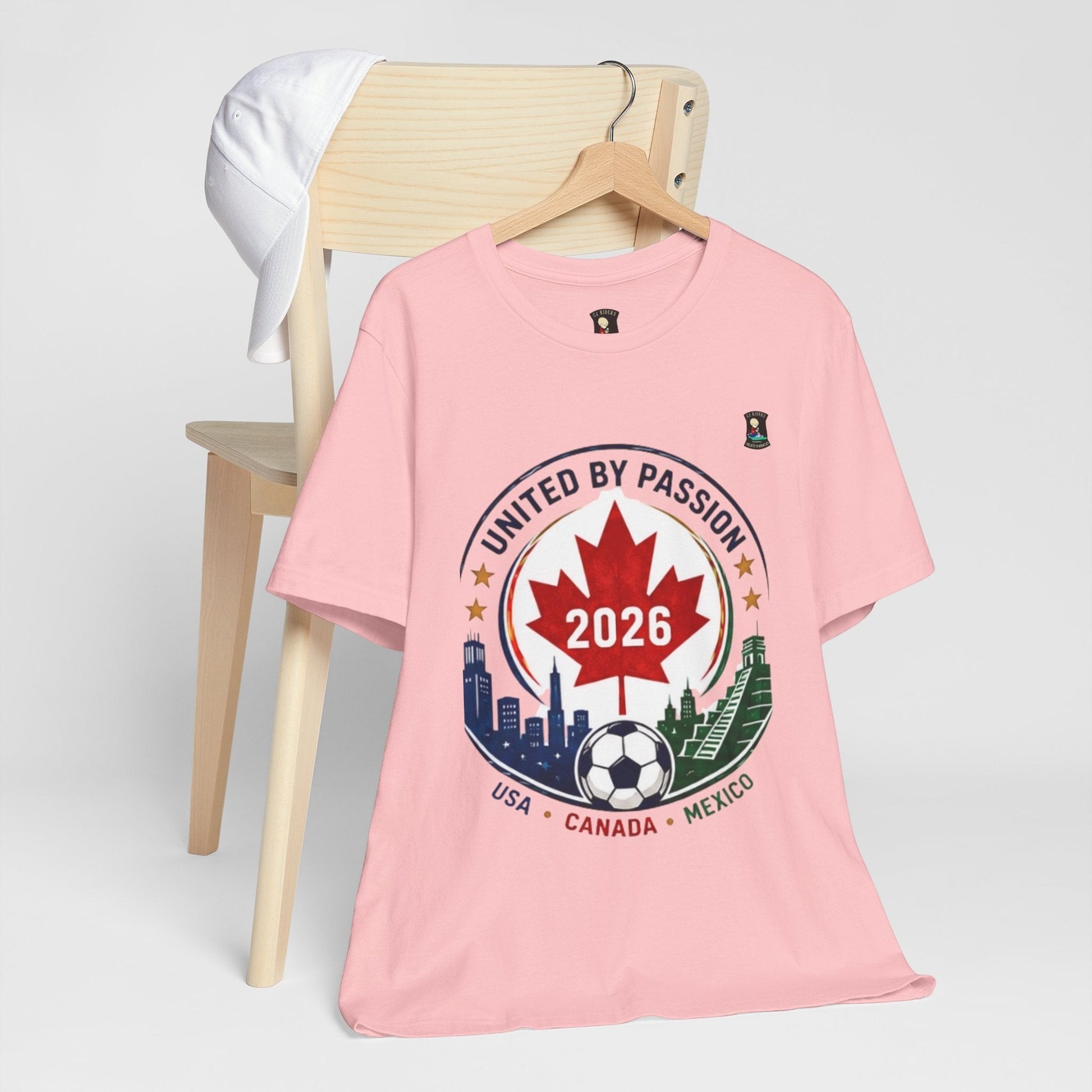 CJ Riders Foundation Store pink 100% cotton t-shirt with a 2026 soccer crest design featuring a Canadian maple leaf, soccer ball, and city skylines.