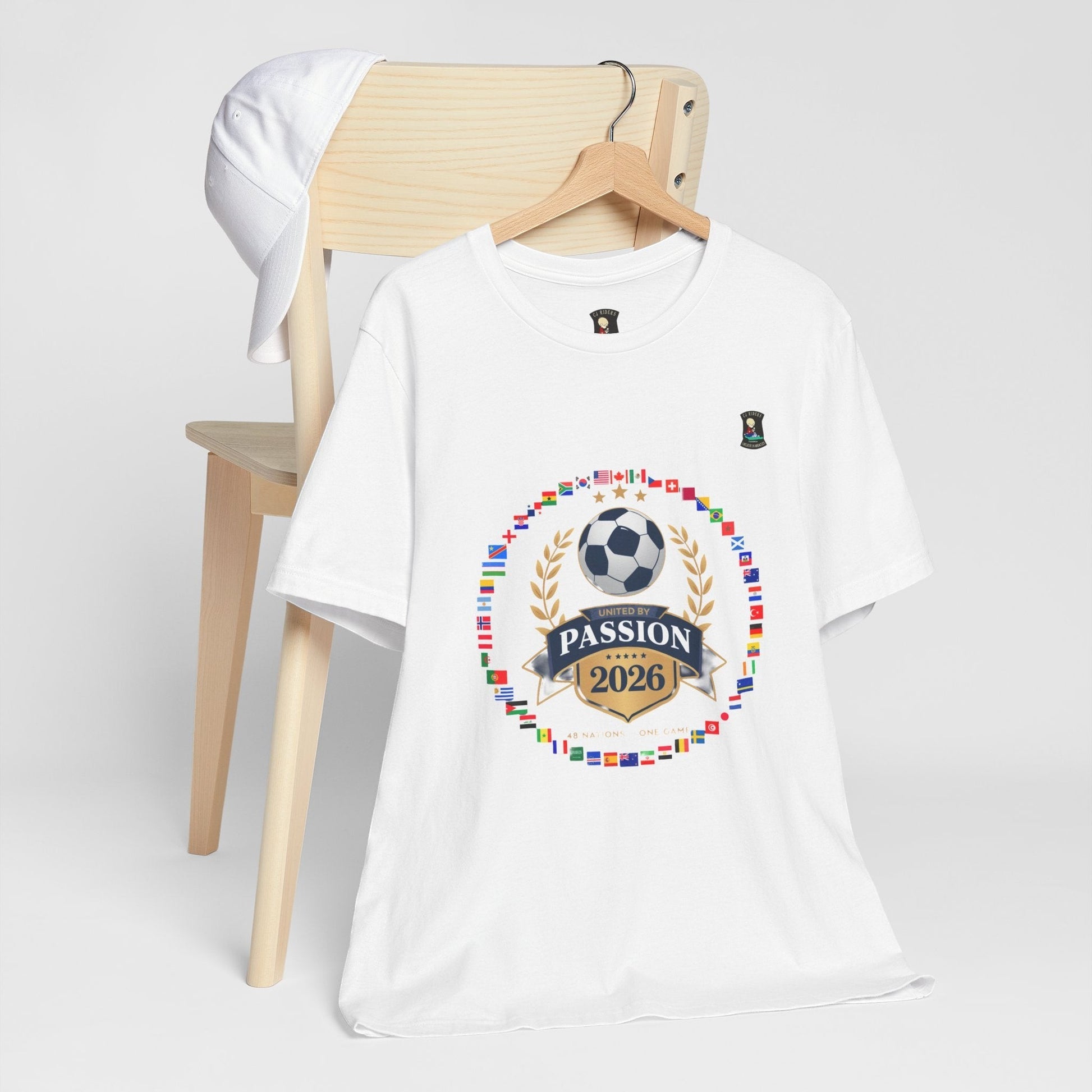 CJ Riders Foundation Store white 100% cotton t-shirt with 2026 soccer graphic featuring flags, a soccer ball, and "United by Passion" text.