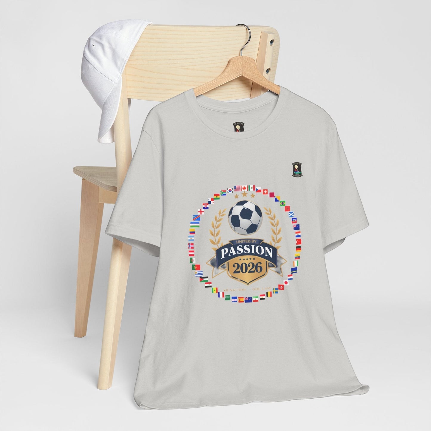 CJ Riders Foundation Store light grey 100% cotton t-shirt with 2026 World Cup graphic featuring flags, soccer ball, and "United by Passion" text.