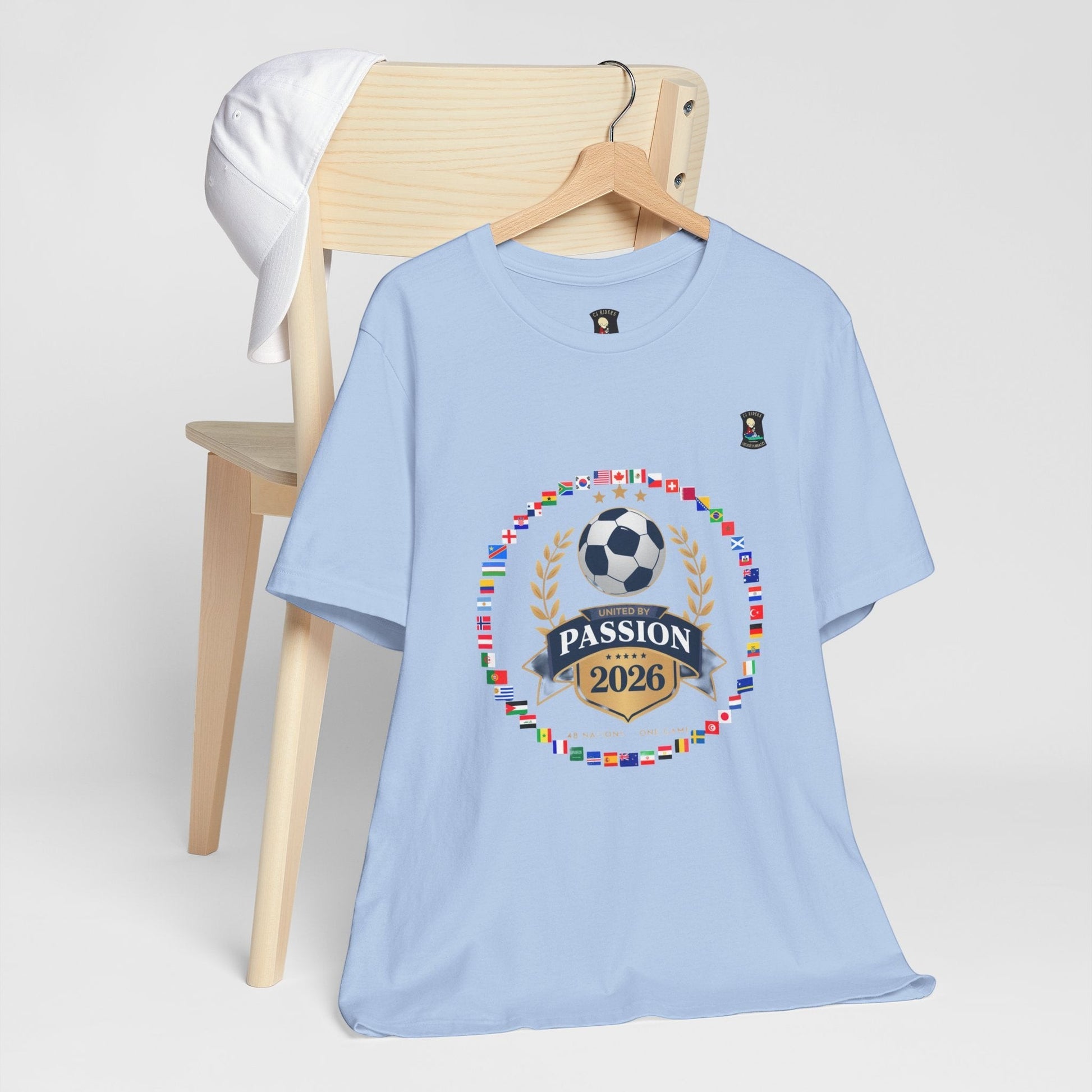 CJ Riders Foundation Store light blue 100% cotton t-shirt with 2026 soccer graphic and international flags.