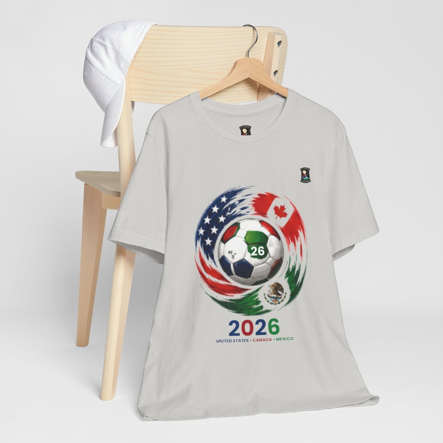 CJ Riders Foundation Store light grey 100% cotton t-shirt with 2026 soccer graphic featuring USA, Canada, and Mexico flags.
