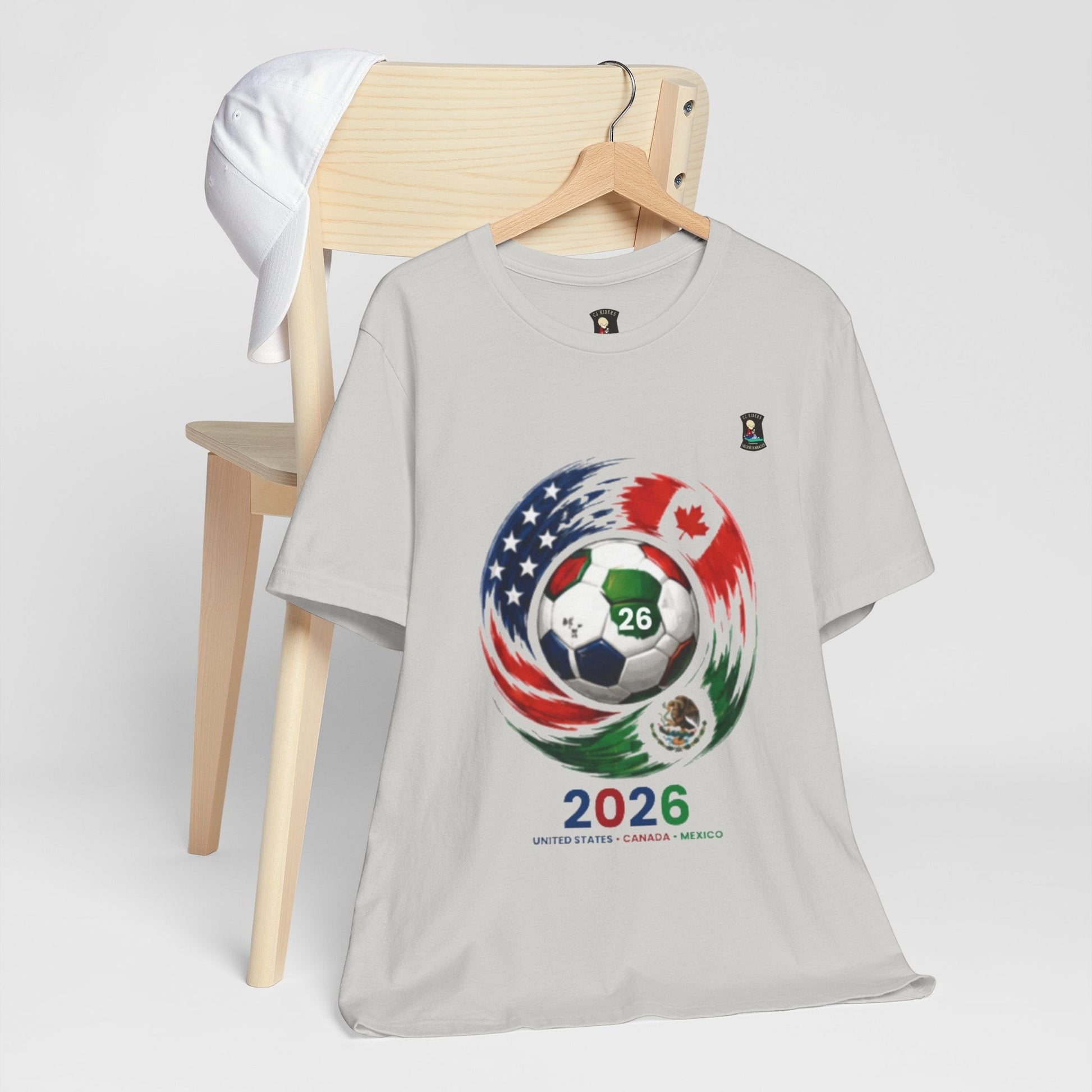 CJ Riders Foundation Store light grey 100% cotton t-shirt with 2026 soccer graphic featuring USA, Canada, and Mexico flags.