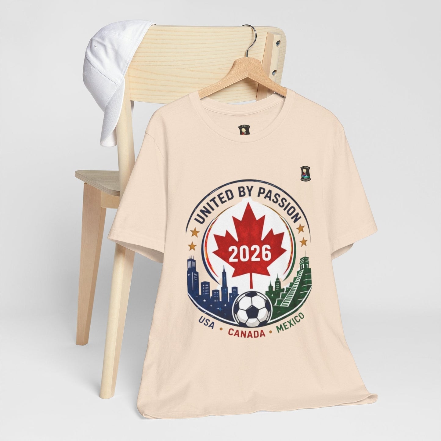 CJ Riders Foundation Store cream 100% cotton t-shirt with 2026 soccer crest design featuring Canada, USA, Mexico.