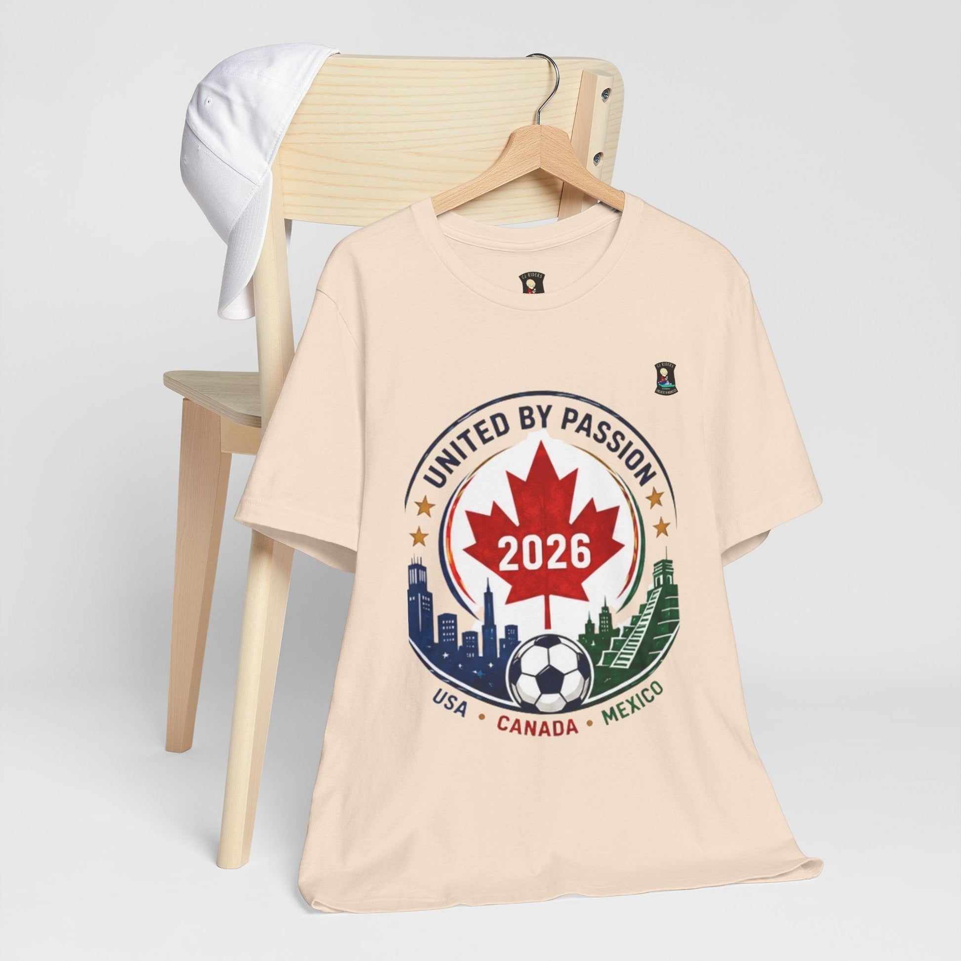 CJ Riders Foundation Store cream 100% cotton t-shirt with 2026 soccer crest design featuring Canada, USA, Mexico.