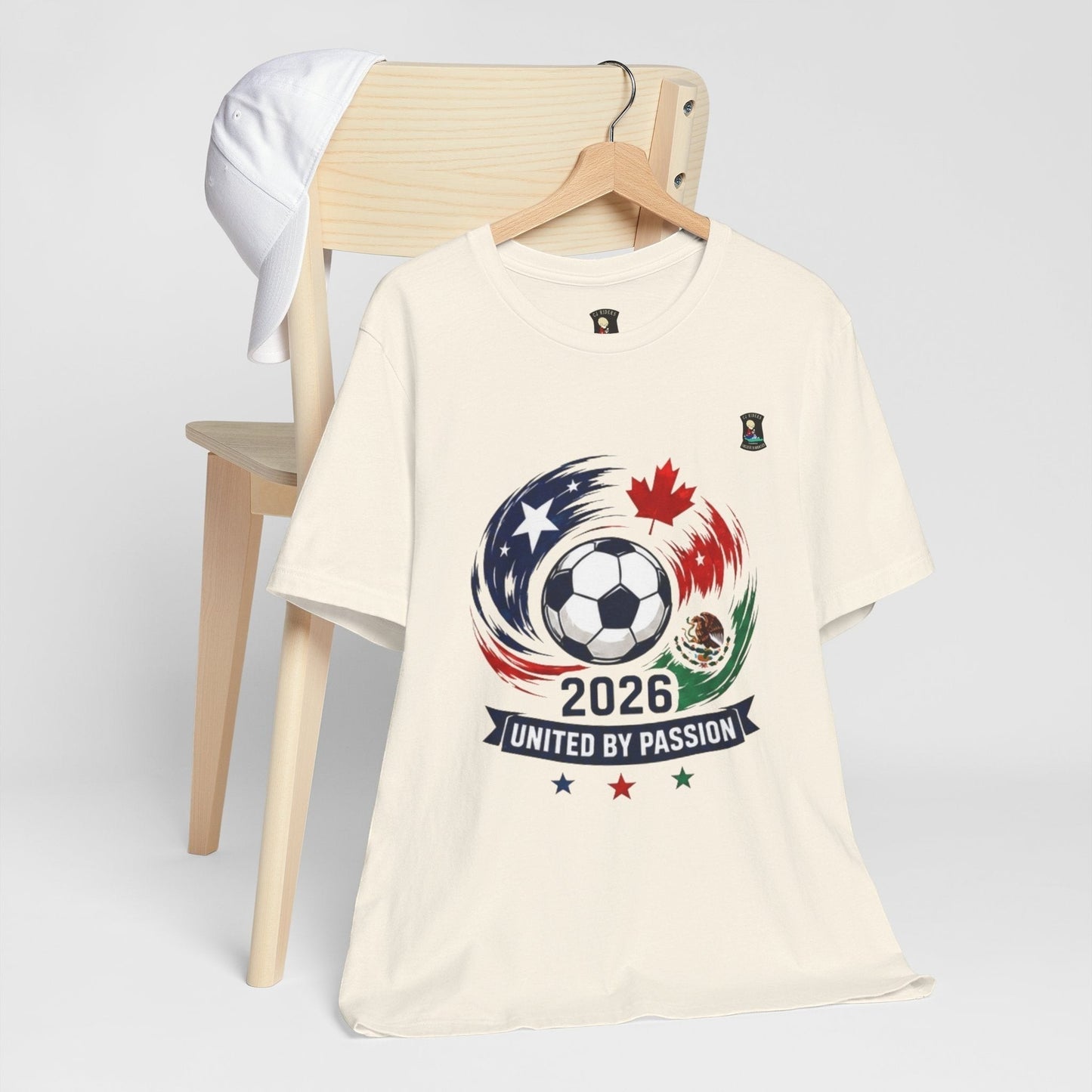 CJ Riders Foundation Store cream 100% cotton t-shirt with 2026 soccer graphic featuring USA, Canada, Mexico flags and ball.