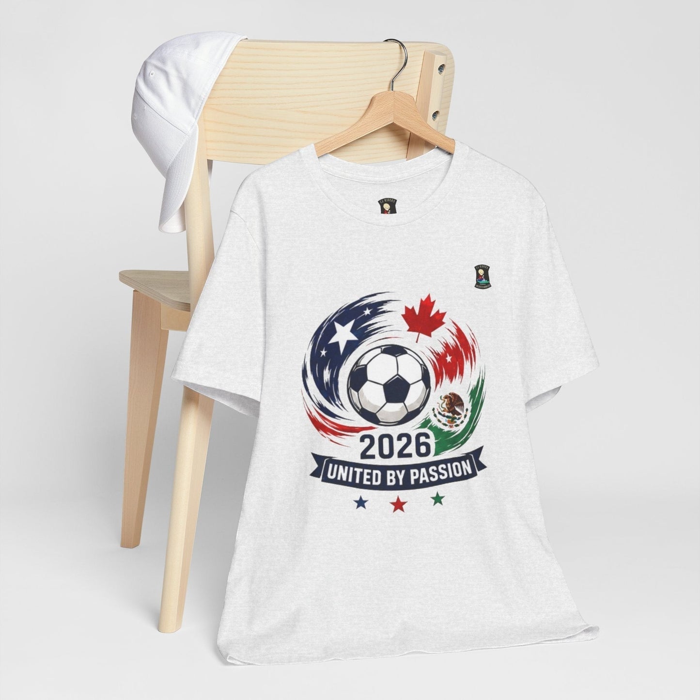 CJ Riders Foundation Store white 100% cotton t-shirt with 2026 soccer graphic, featuring a ball, USA, Canada, Mexico flags, and "United by Passion" text.