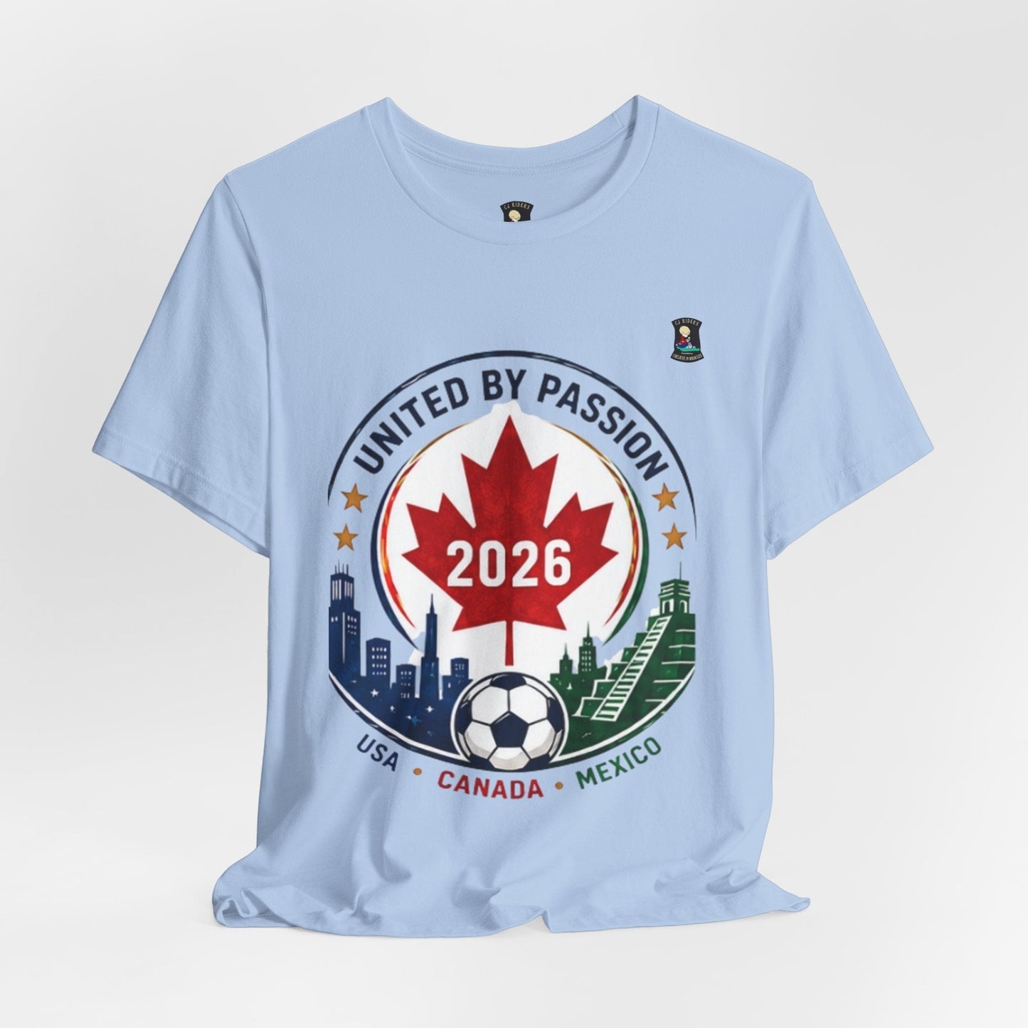 CJ Riders Foundation Store light blue 100% cotton t-shirt with a circular graphic celebrating the 2026 World Cup, featuring a Canadian maple leaf, soccer ball, and skylines of USA, Canada, and Mexico.