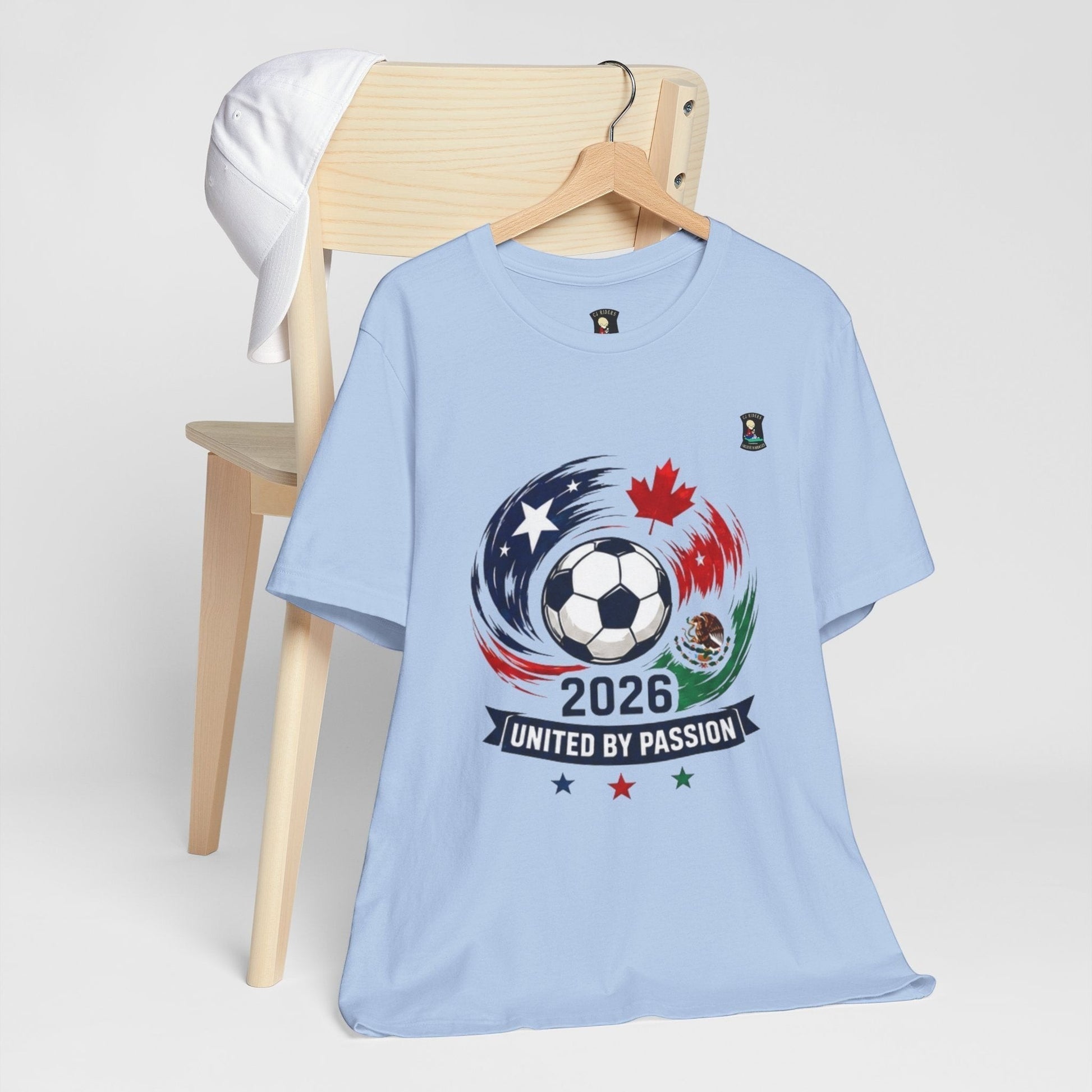 CJ Riders Foundation Store light blue 100% cotton soccer t-shirt with 2026 United by Passion graphic featuring a soccer ball, USA, Canada, and Mexico flags.