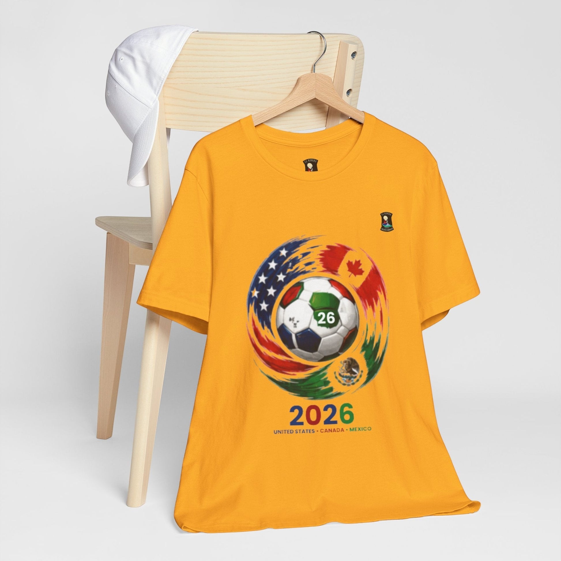 CJ Riders Foundation Store yellow 100% cotton t-shirt with 2026 World Cup graphic featuring soccer ball, USA, Canada, Mexico flags.