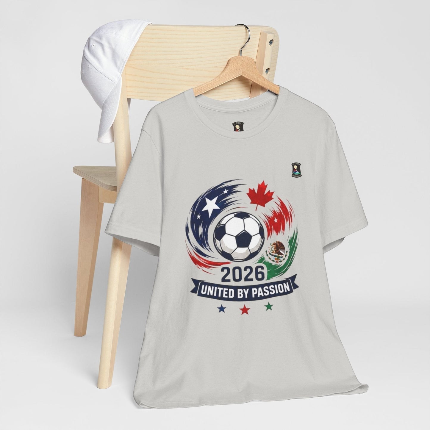 CJ Riders Foundation Store light grey 100% cotton t-shirt with 2026 soccer ball graphic, USA, Canada, Mexico flags and "United by Passion" text.