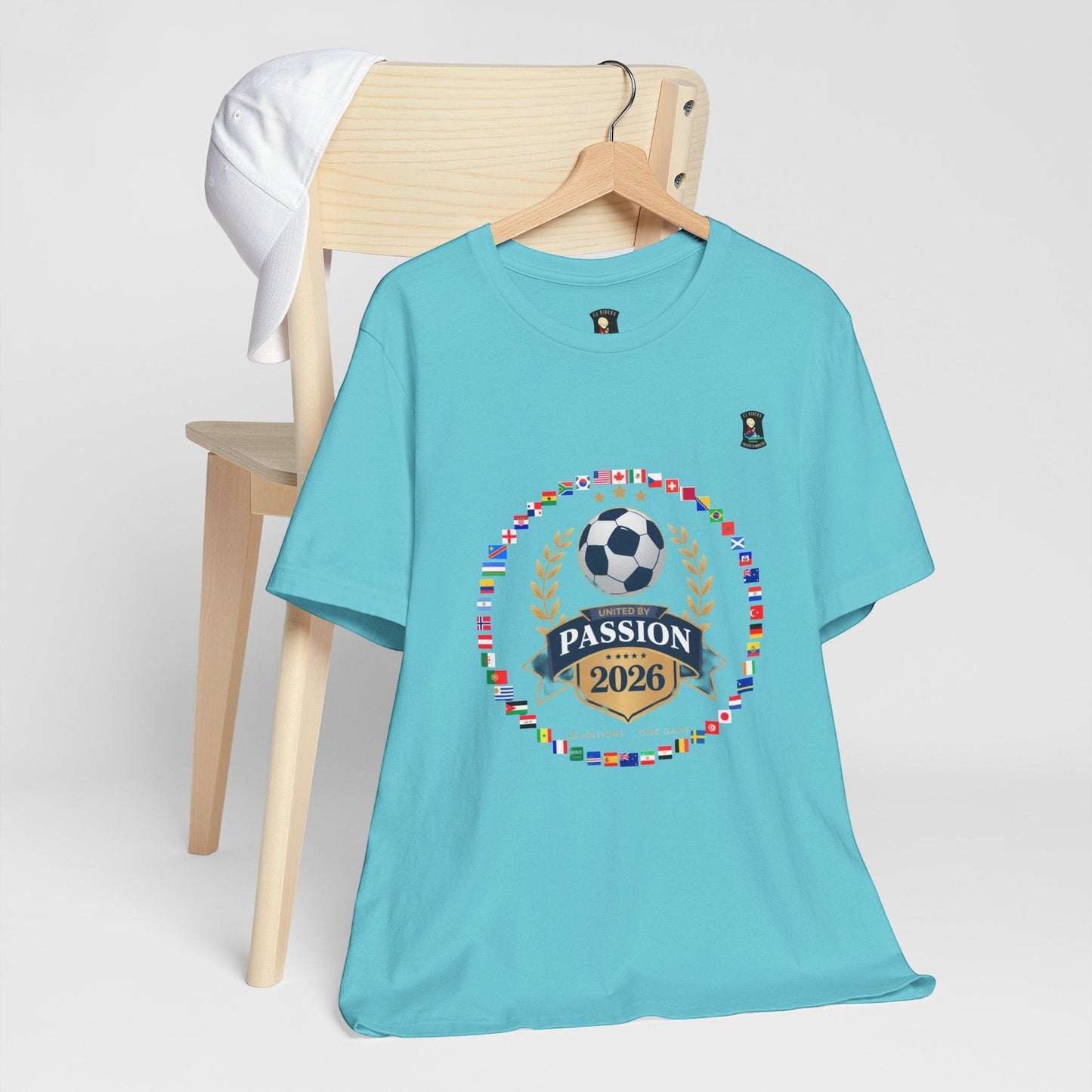 CJ Riders Foundation Store turquoise 100% cotton t-shirt with 2026 World Cup graphic featuring flags, soccer ball, and "United by Passion" text.