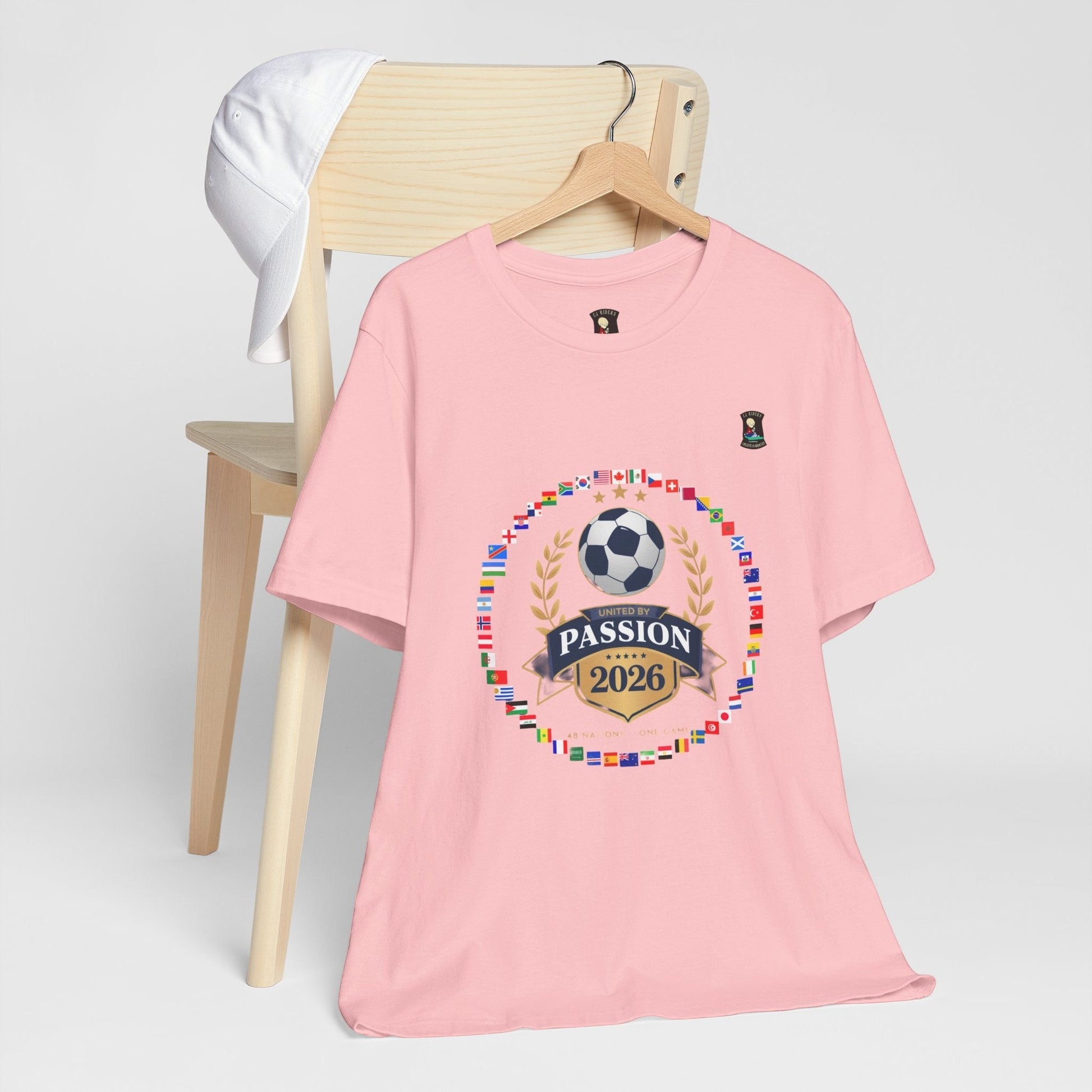 CJ Riders Foundation Store pink 100% cotton t-shirt with 2026 World Cup graphic featuring a soccer ball, flags, and "United by Passion" text.
