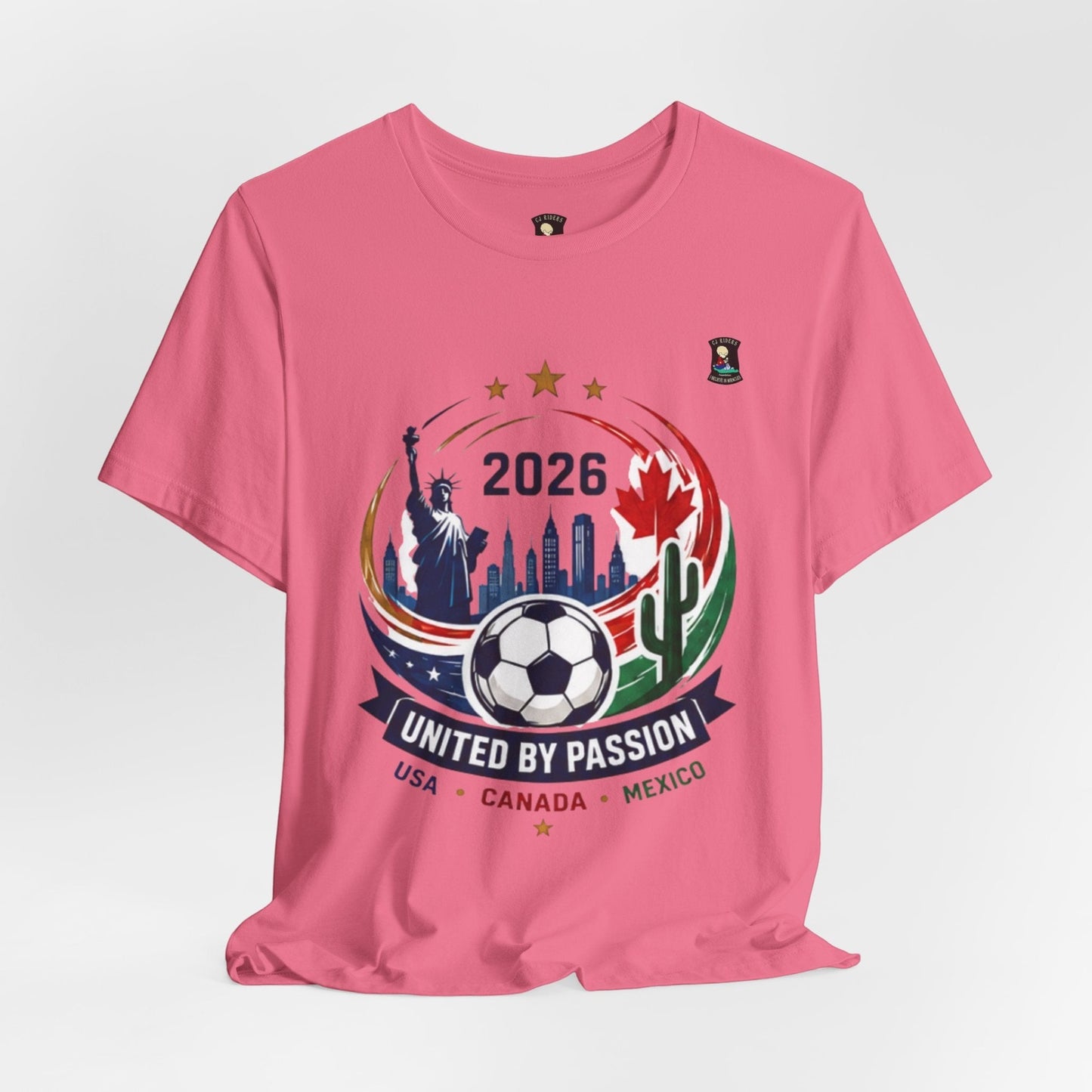 CJ Riders Foundation Store pink 100% cotton t-shirt with 2026 soccer graphic featuring Statue of Liberty, Canadian maple leaf, Mexican cactus, and soccer ball.