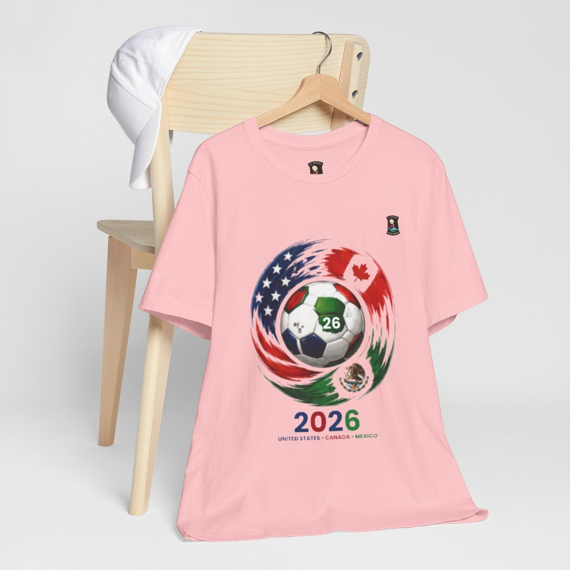 CJ Riders Foundation Store pink 100% cotton t-shirt with 2026 World Cup graphic featuring a soccer ball and flags of USA, Canada, and Mexico.