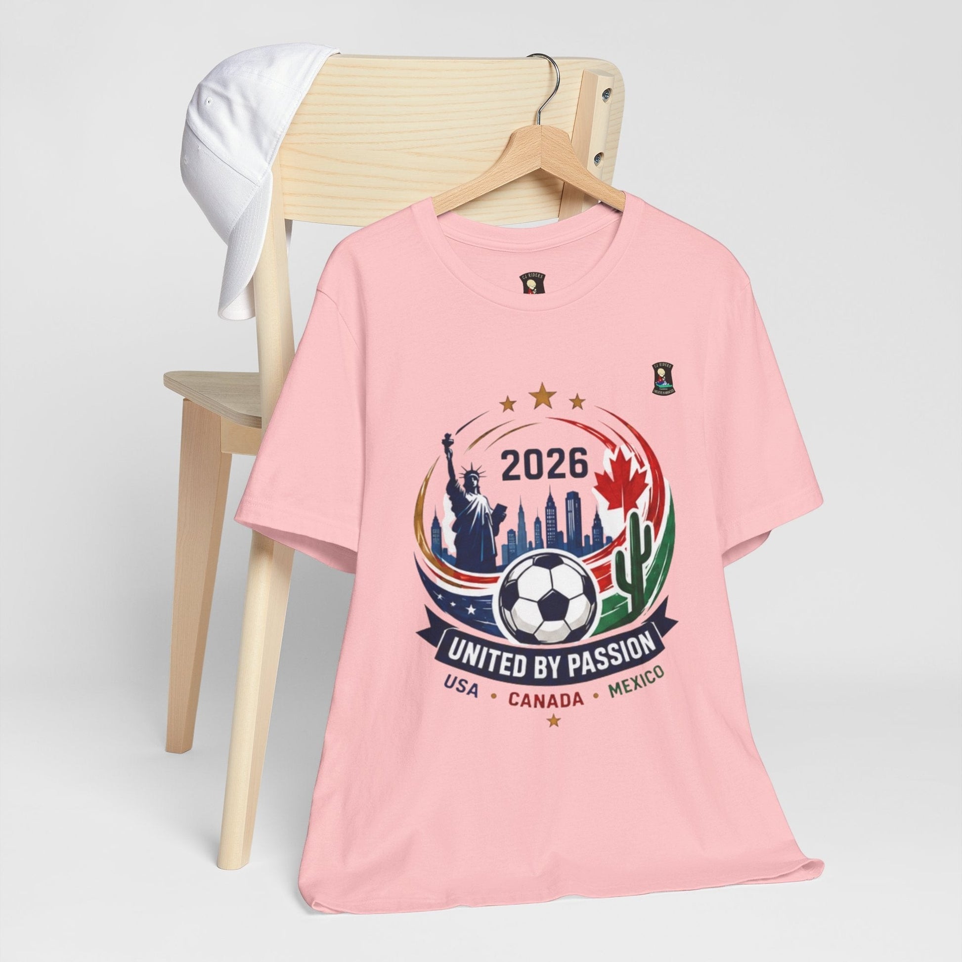 CJ Riders Foundation Store pink 100% cotton t-shirt with 2026 soccer graphic featuring USA, Canada, Mexico landmarks and a soccer ball.