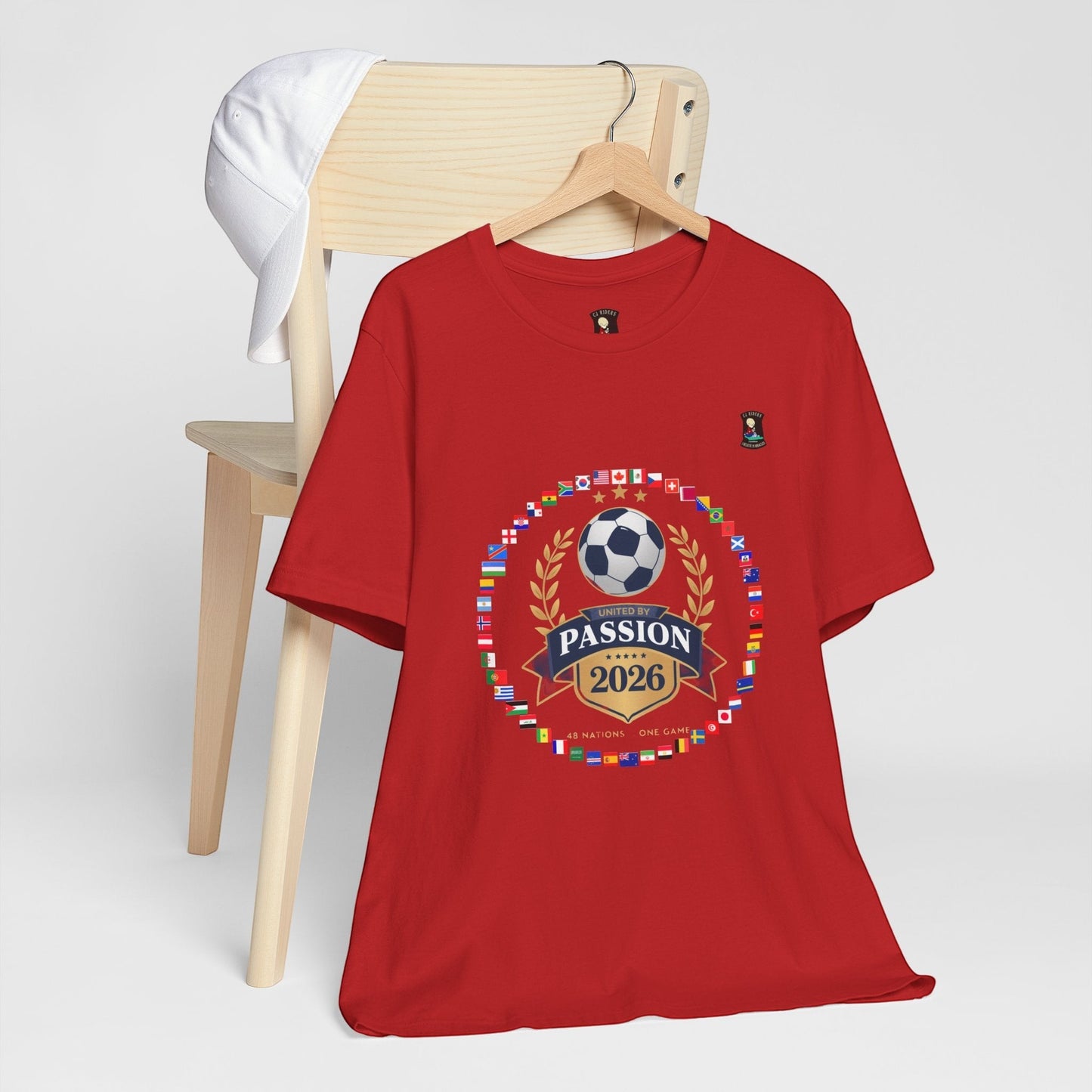 CJ Riders Foundation Store red 100% cotton t-shirt with 2026 soccer graphic featuring flags, a soccer ball, and "United by Passion" text.