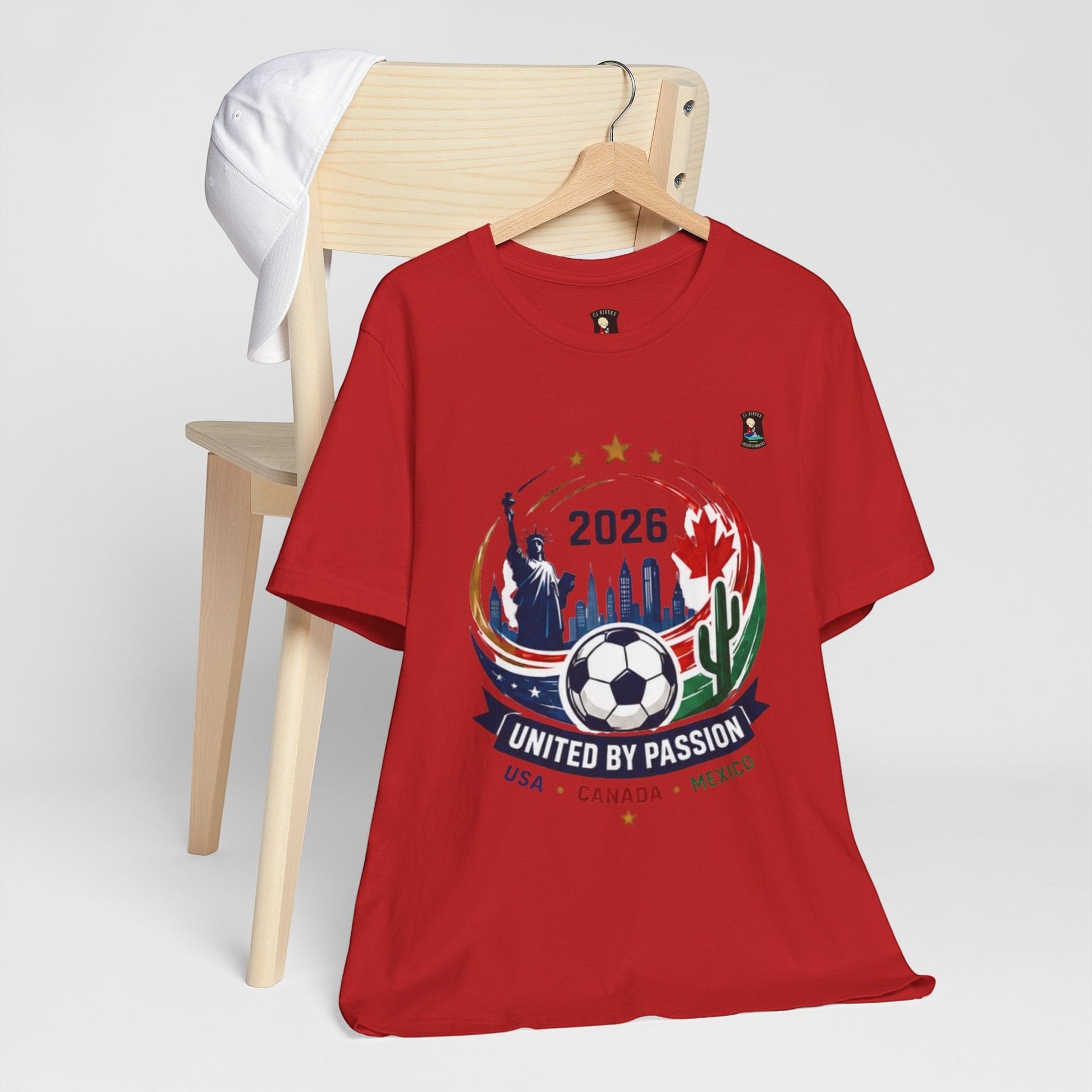 CJ Riders Foundation Store red 100% cotton t-shirt with 2026 soccer graphic featuring USA, Canada, Mexico, Statue of Liberty, and soccer ball.