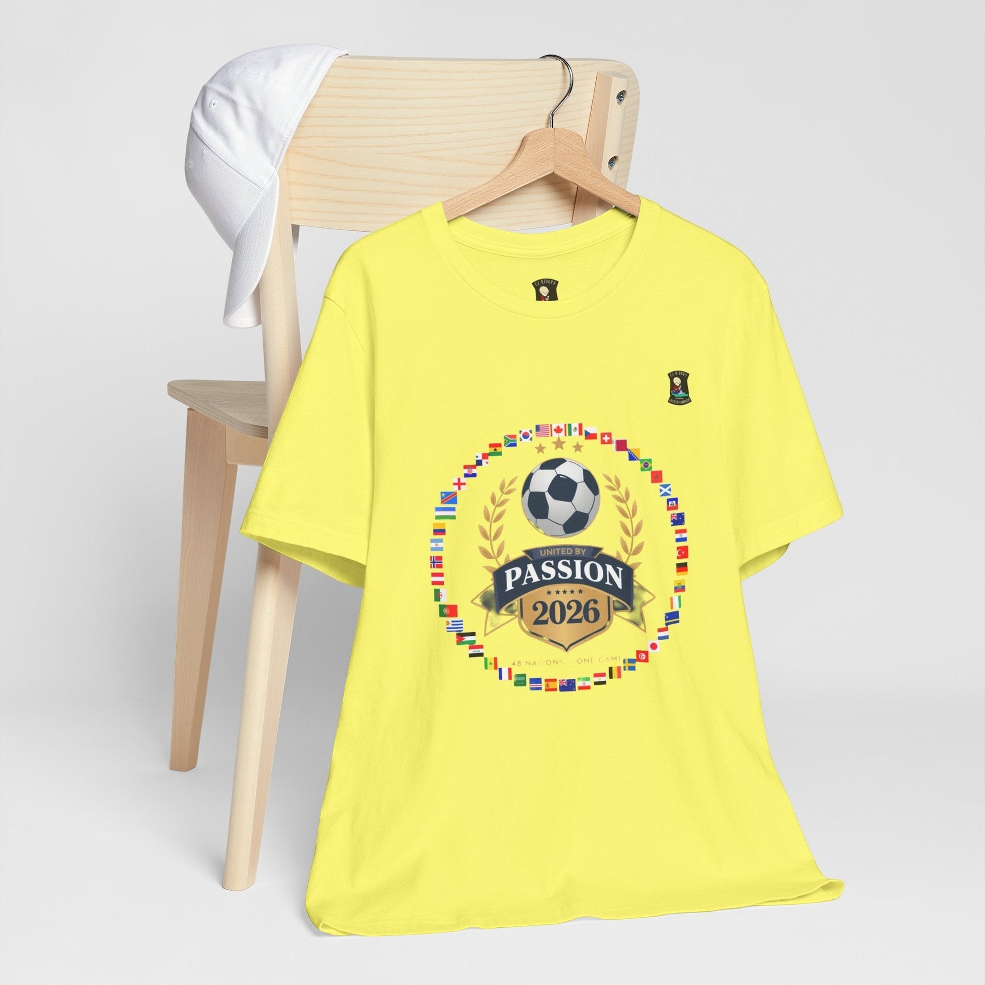 CJ Riders Foundation Store yellow 100% cotton t-shirt with 2026 World Cup graphic featuring flags, soccer ball, and "United by Passion" text.