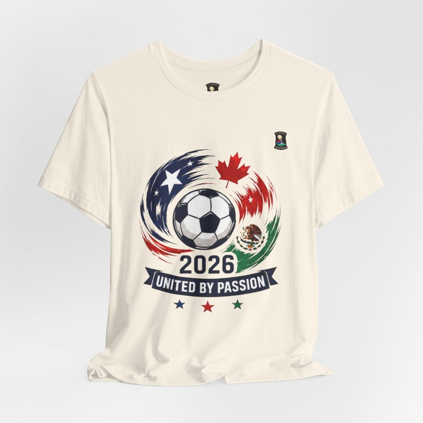 CJ Riders Foundation Store cream 100% cotton t-shirt with 2026 soccer graphic featuring a ball, USA, Canada, Mexico flags, and "United by Passion" text.