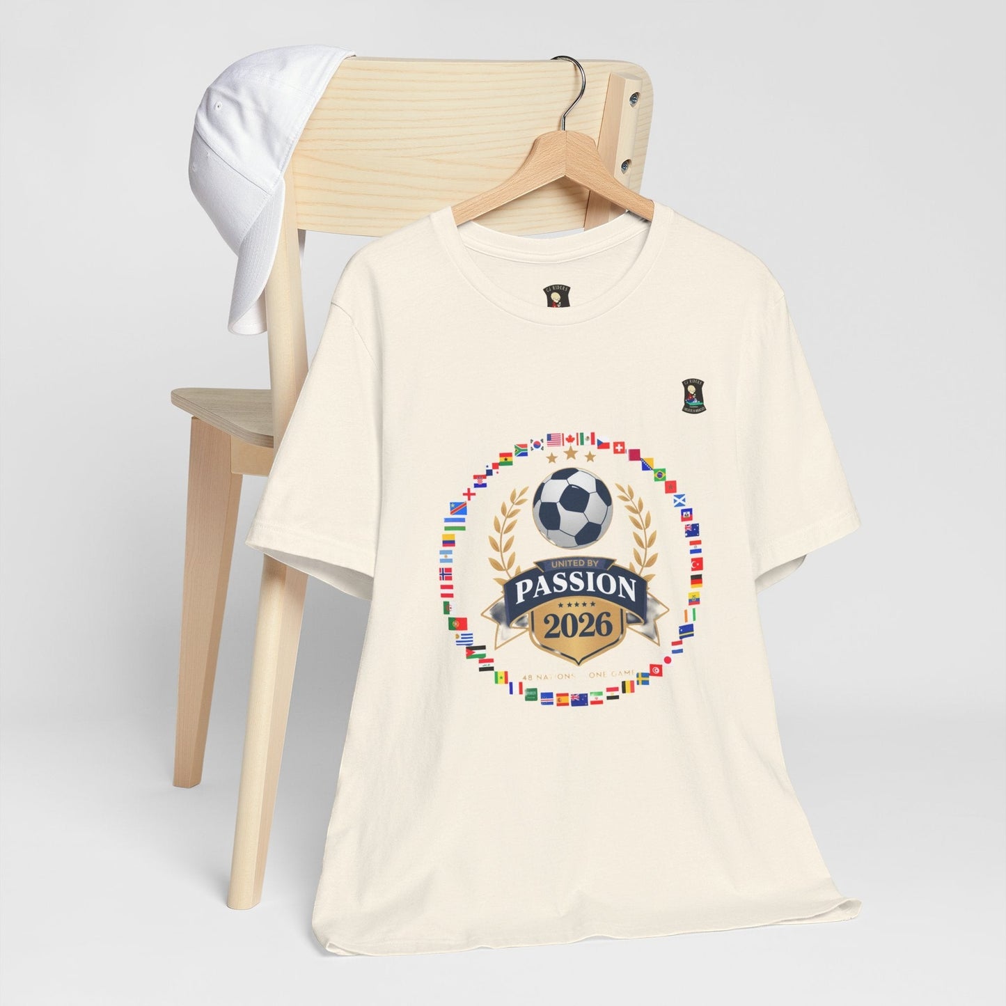 CJ Riders Foundation Store cream 100% cotton t-shirt with 2026 World Cup graphic featuring flags, soccer ball, and "United by Passion" text.