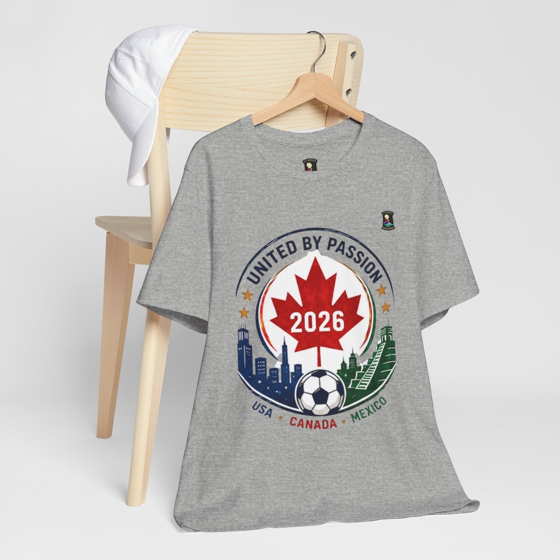 CJ Riders Foundation Store grey 100% cotton t-shirt with 2026 soccer crest design featuring Canadian maple leaf, soccer ball, and city skylines.