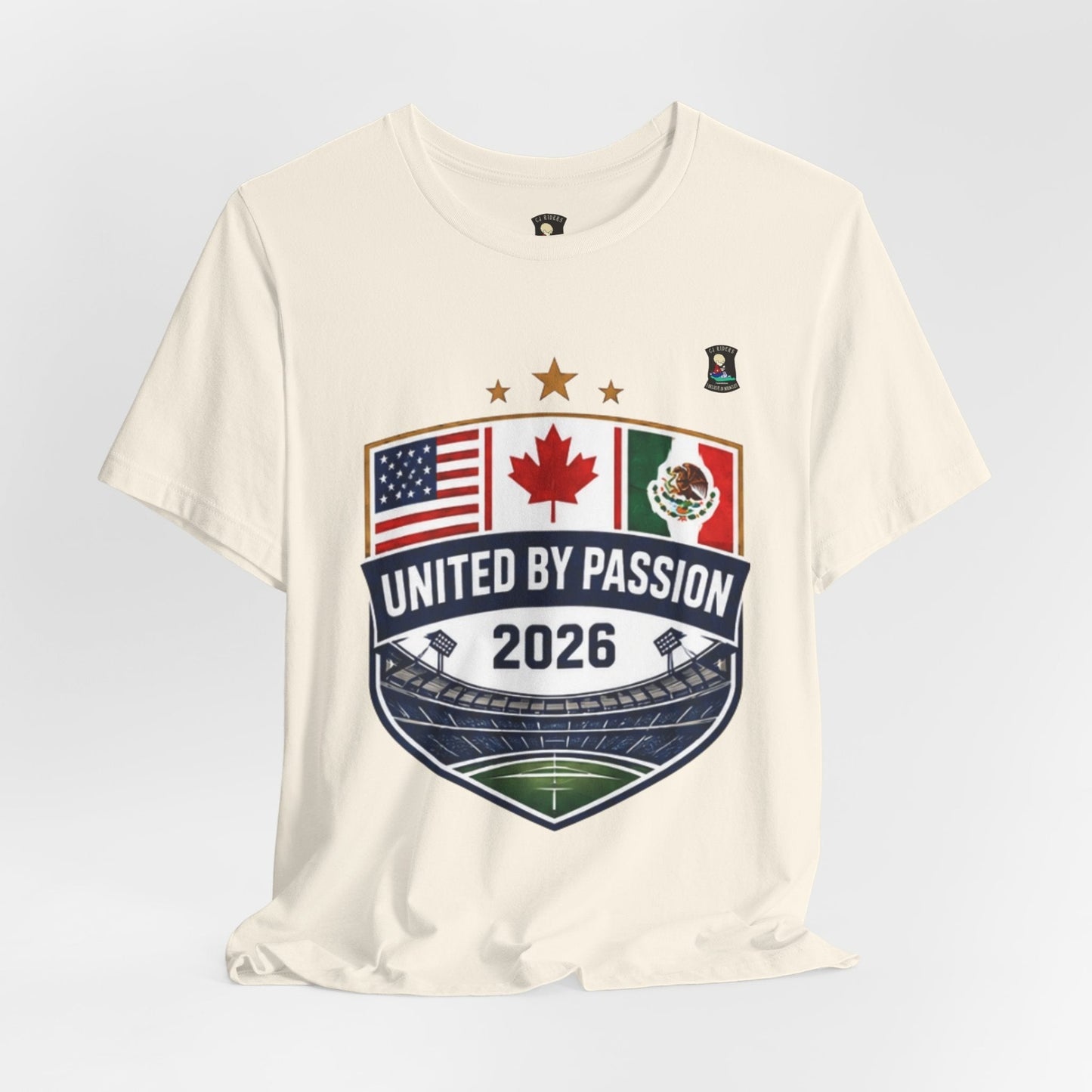 Cream 100% cotton t-shirt with a shield design featuring USA, Canada, and Mexico flags, "United by Passion 2026" text, and stadium graphic. CJ Riders Foundation Store.