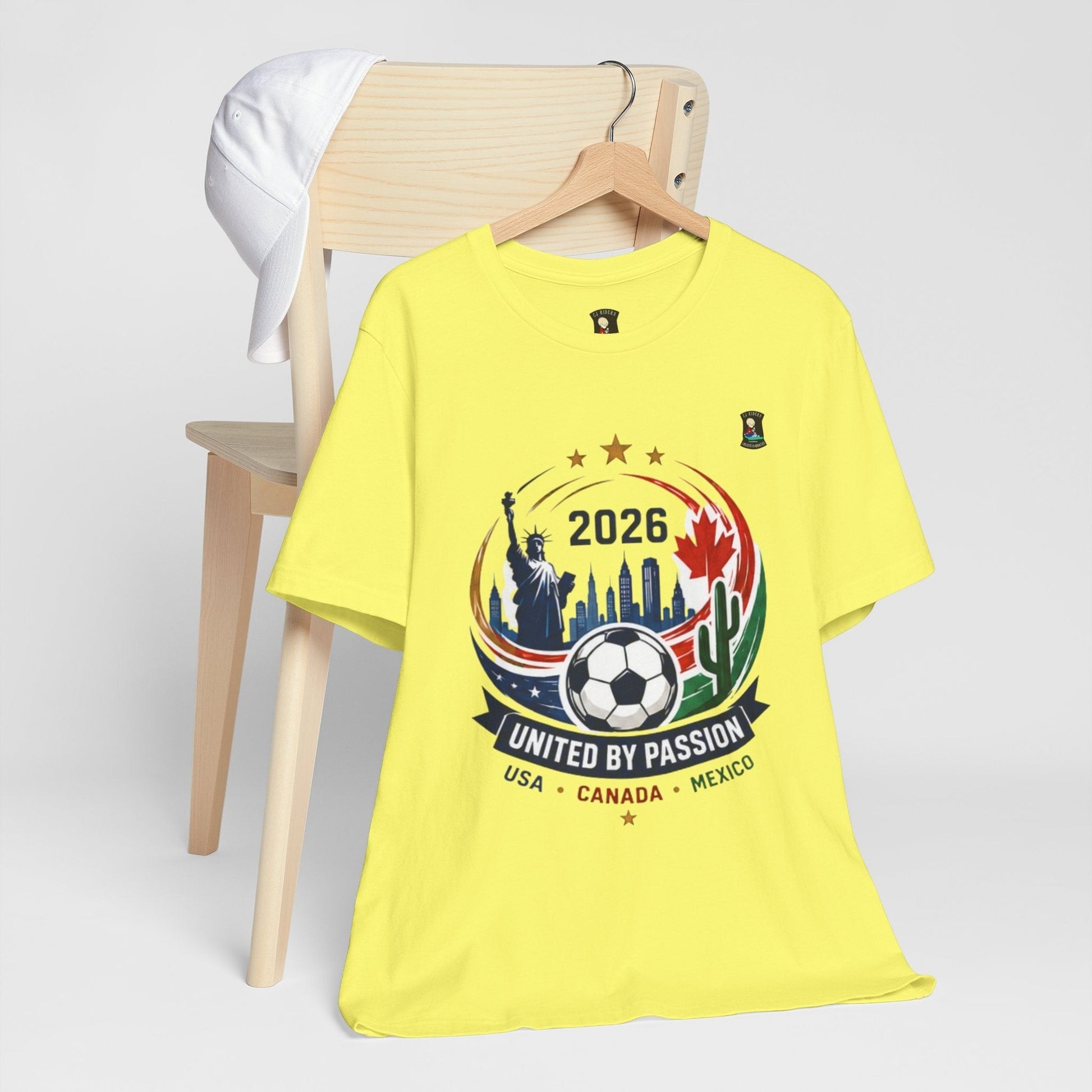 CJ Riders Foundation Store yellow 100% cotton t-shirt with 2026 soccer graphic featuring USA, Canada, Mexico landmarks and soccer ball.