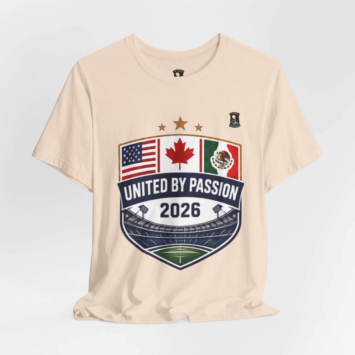 CJ Riders Foundation Store cream 100% cotton t-shirt with United by Passion 2026 shield design featuring USA, Canada, Mexico flags and stadium graphic.
