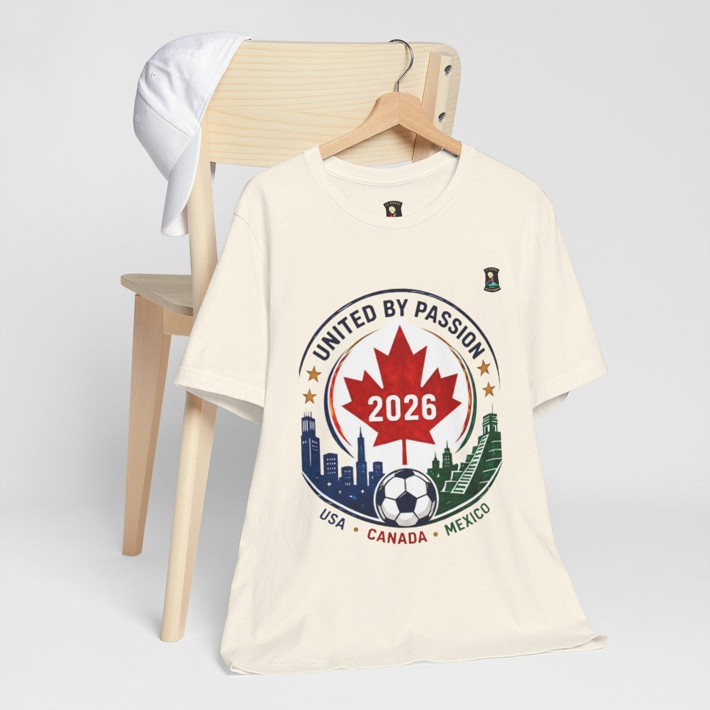 CJ Riders Foundation Store cream 100% cotton t-shirt with United by Passion 2026 soccer graphic. Features Canadian maple leaf, soccer ball, and city skylines.