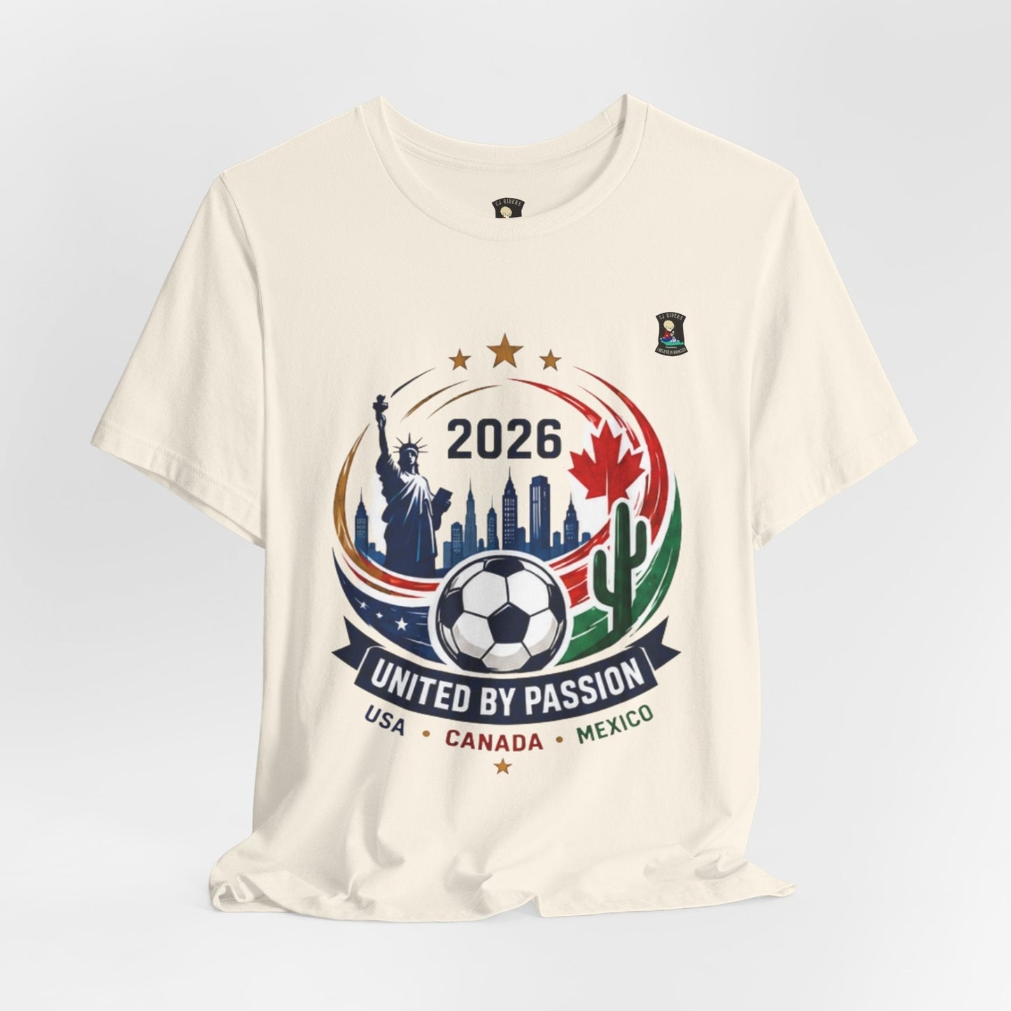 Cream 100% cotton t-shirt with United by Passion 2026 soccer graphic featuring Statue of Liberty, cityscape, soccer ball, maple leaf, cactus, and USA, Canada, Mexico text.