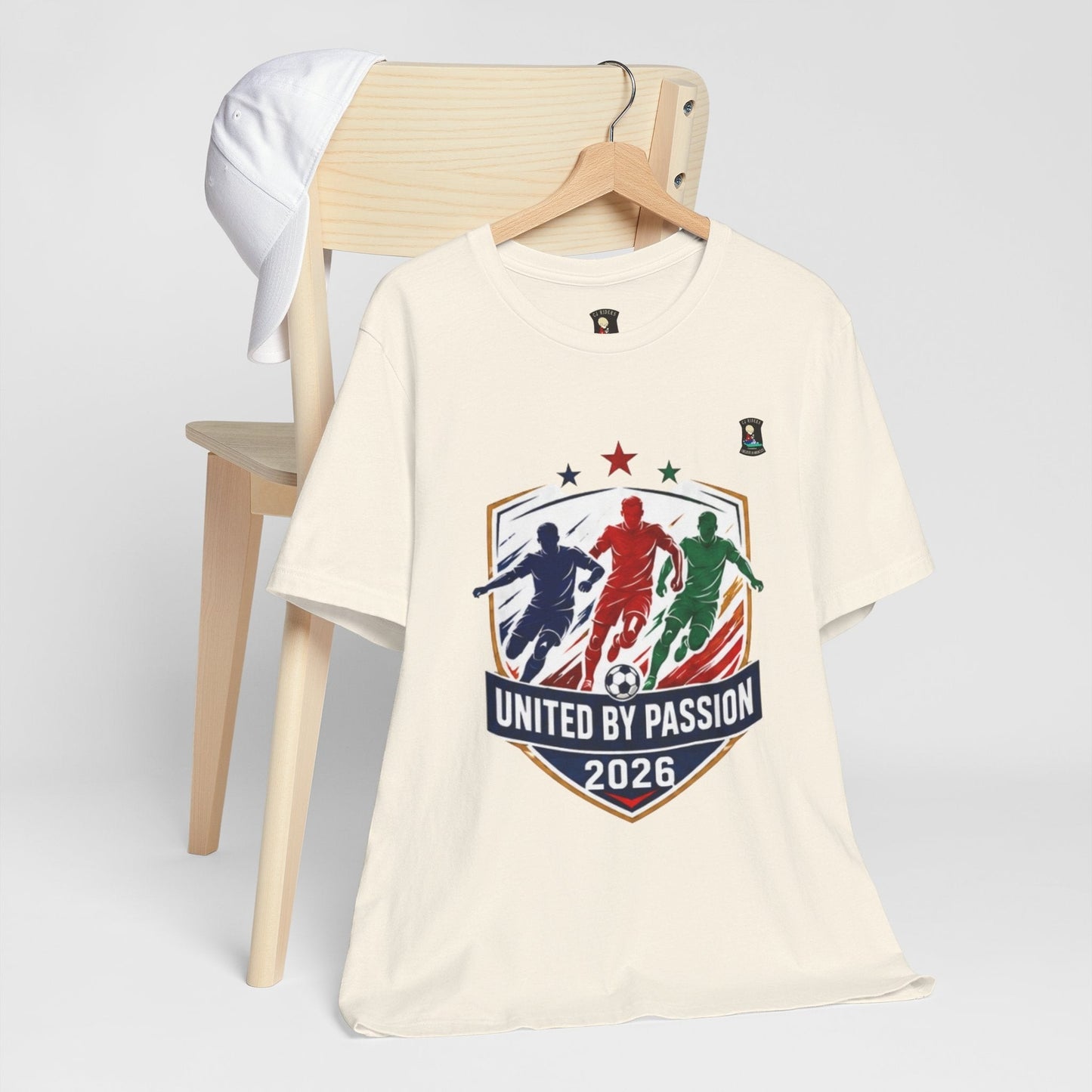 CJ Riders Foundation Store cream 100% cotton t-shirt with "United by Passion 2026" soccer graphic featuring three players.