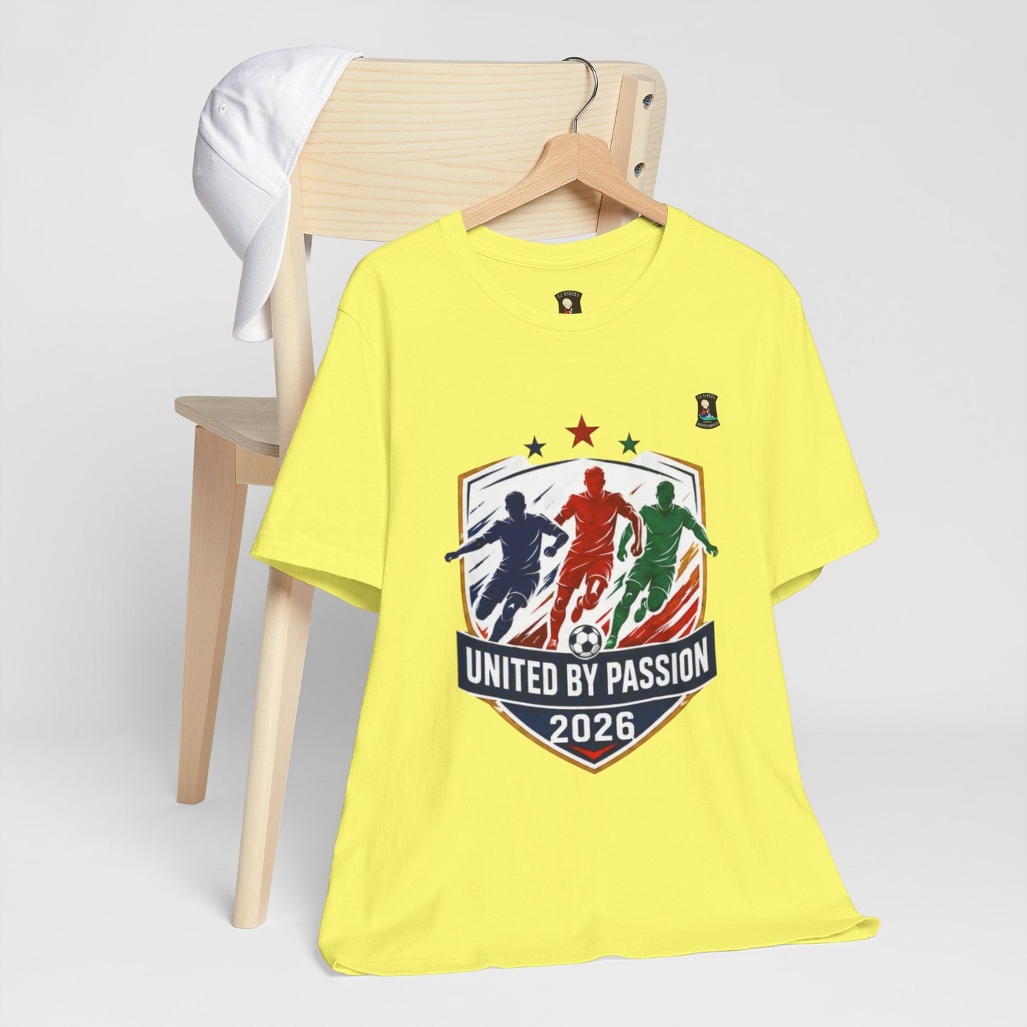 CJ Riders Foundation Store yellow cotton t-shirt with "United by Passion 2026" soccer graphic featuring three players.