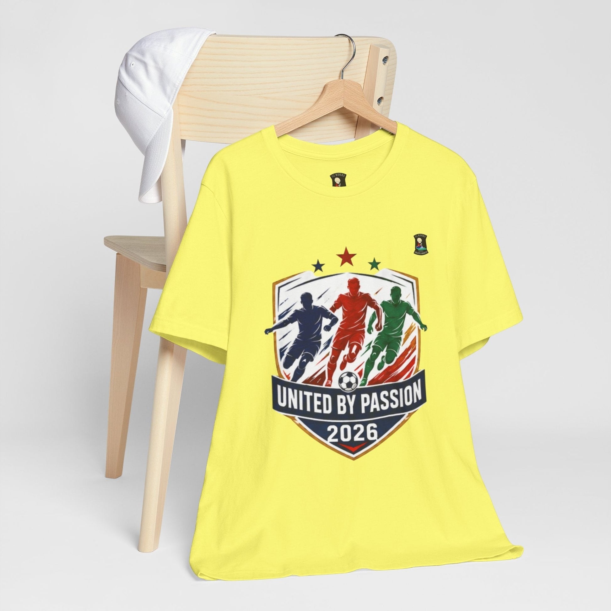 CJ Riders Foundation Store yellow cotton t-shirt with "United by Passion 2026" soccer graphic featuring three players.