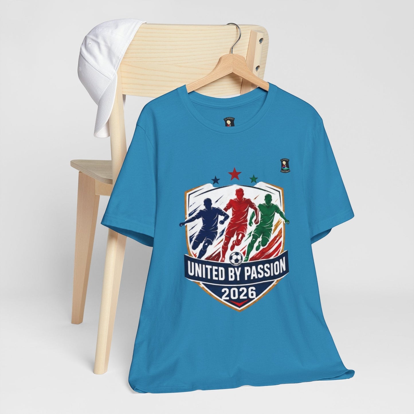 CJ Riders Foundation Store blue 100% cotton t-shirt with "United by Passion 2026" graphic featuring three soccer players and a ball.