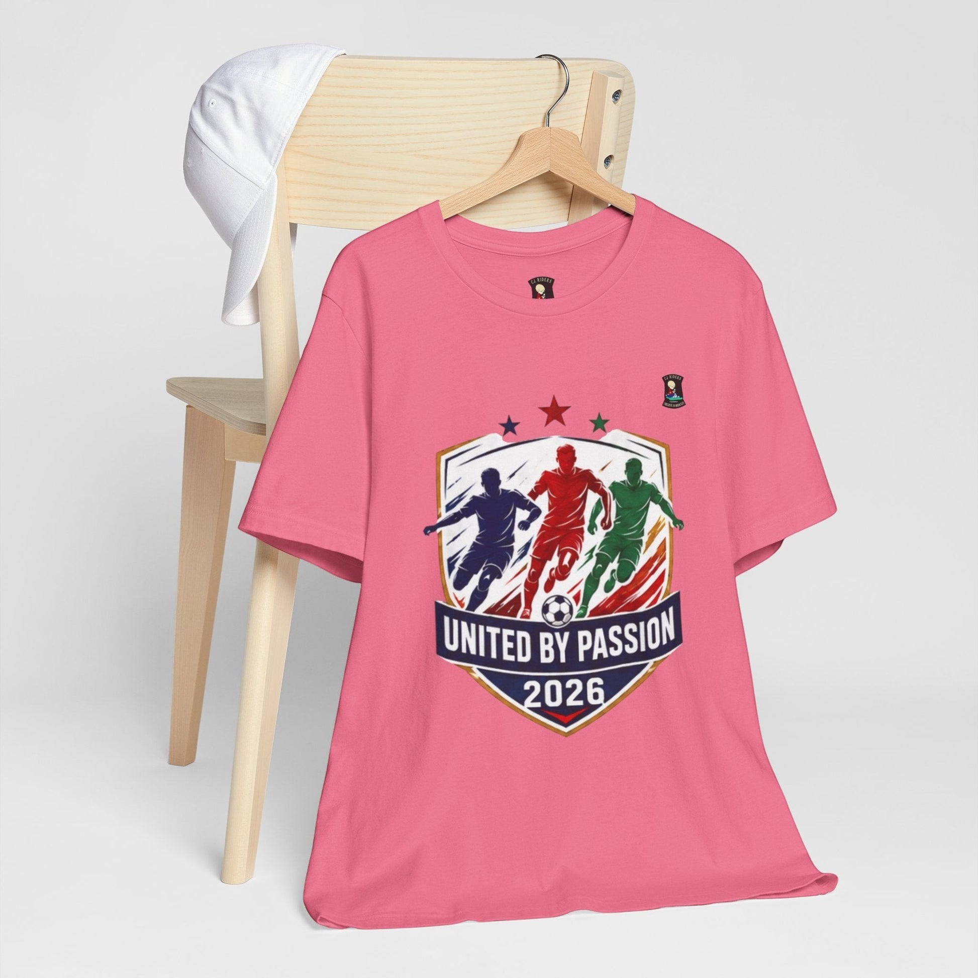 CJ Riders Foundation Store pink cotton t-shirt with "United by Passion 2026" soccer graphic featuring three players and a ball.