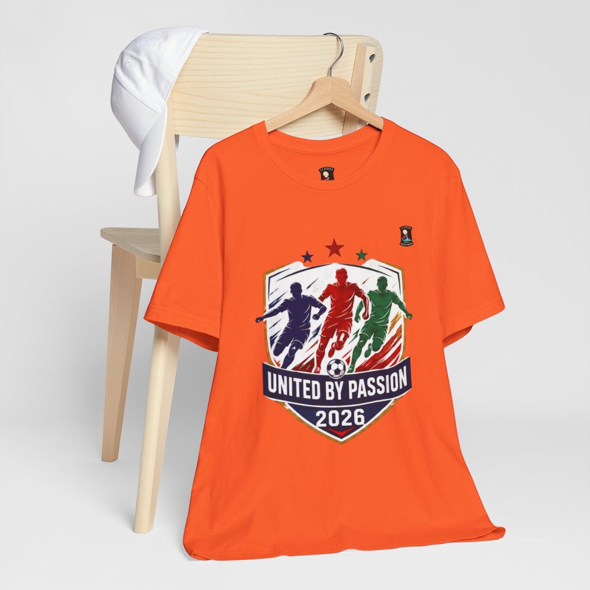 CJ Riders Foundation Store orange 100% cotton t-shirt with "United by Passion 2026" soccer graphic.