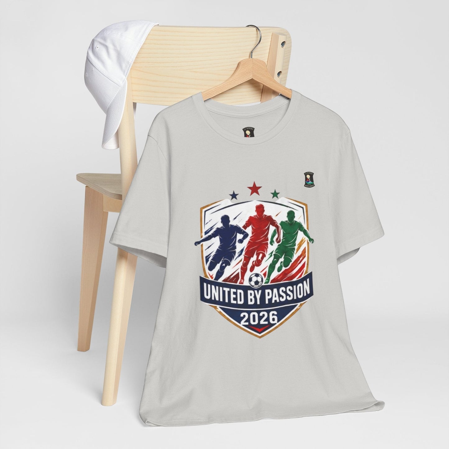 CJ Riders Foundation Store light grey 100% cotton t-shirt with "United by Passion 2026" soccer graphic featuring three players and a ball.