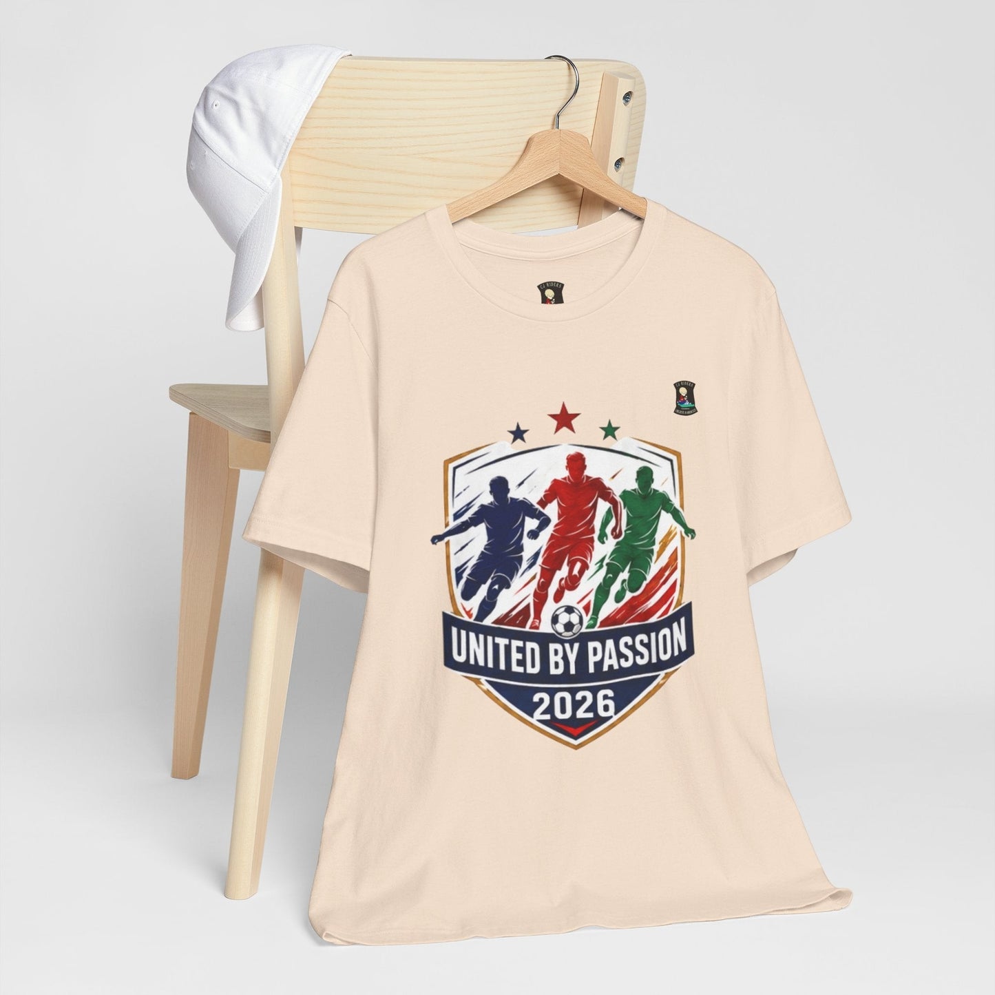 CJ Riders Foundation Store cream 100% cotton t-shirt with "United by Passion 2026" soccer graphic featuring three players.