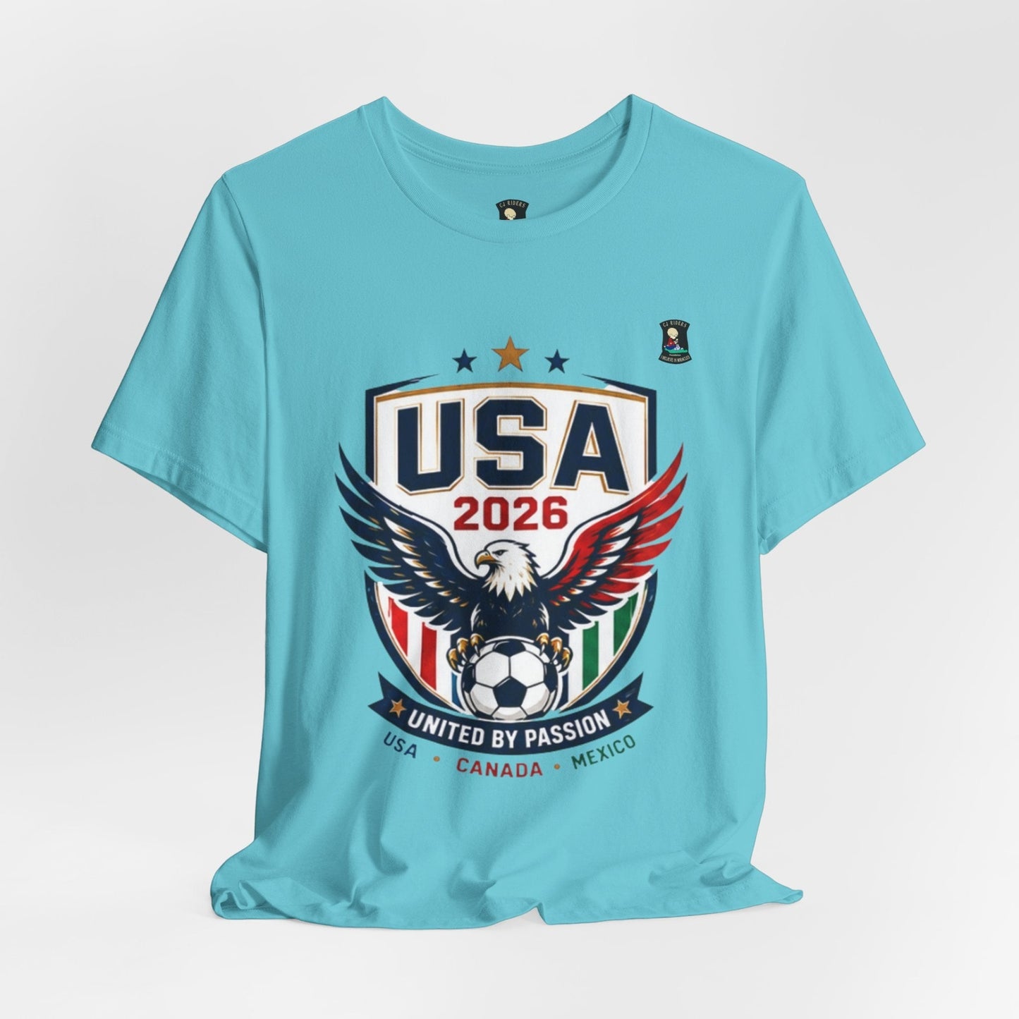 CJ Riders Foundation Store light blue 100% cotton t-shirt with USA 2026 eagle and soccer ball graphic. Features "United by Passion" text.