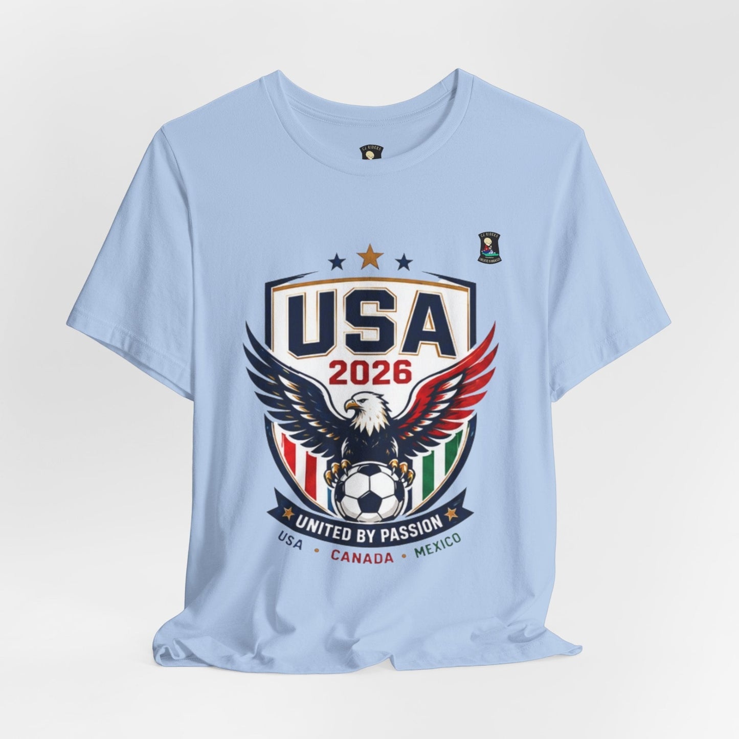 CJ Riders Foundation Store light blue 100% cotton USA 2026 soccer t-shirt with eagle graphic and "United by Passion" text.