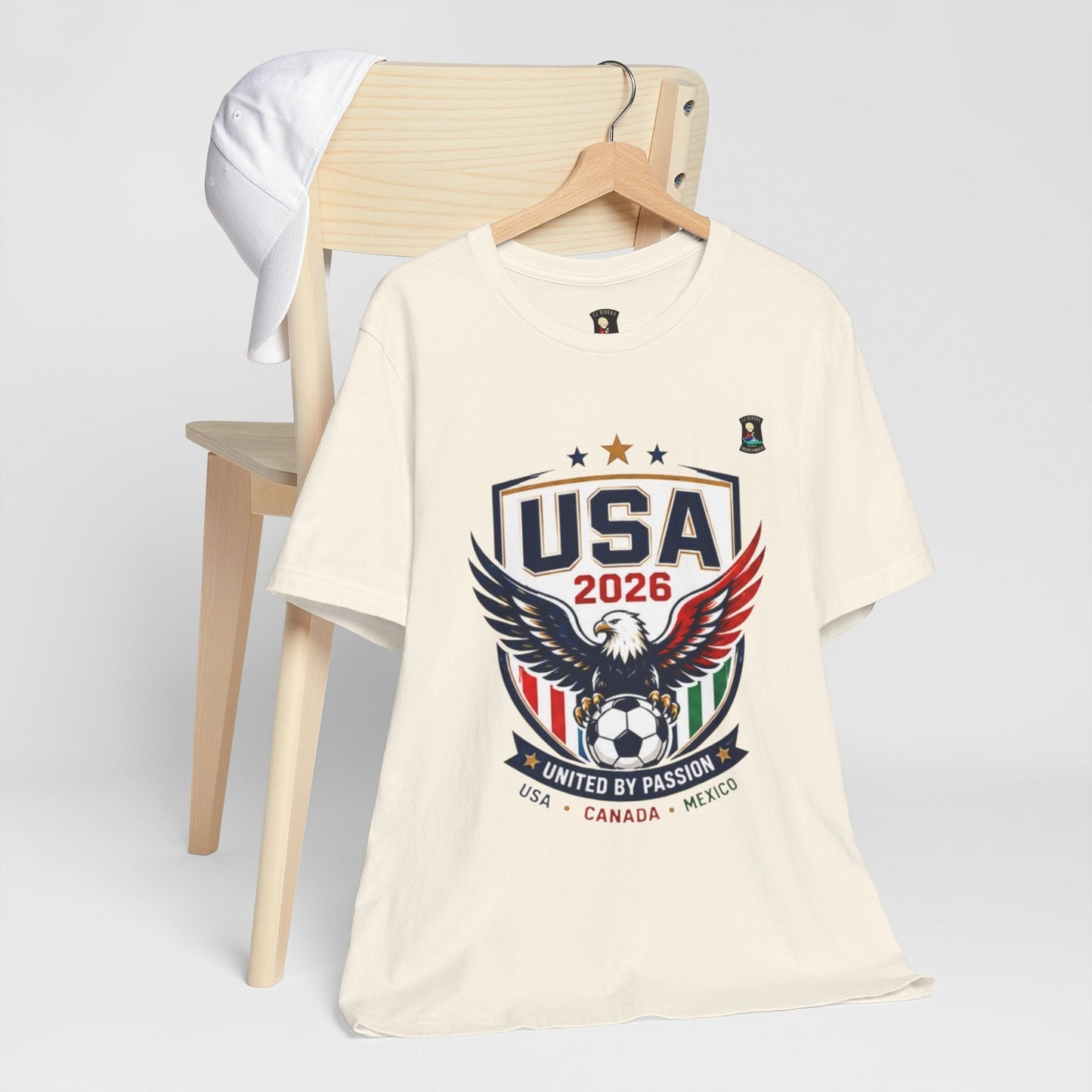 CJ Riders Foundation Store cream 100% cotton USA 2026 soccer t-shirt with eagle graphic and "United by Passion" text.