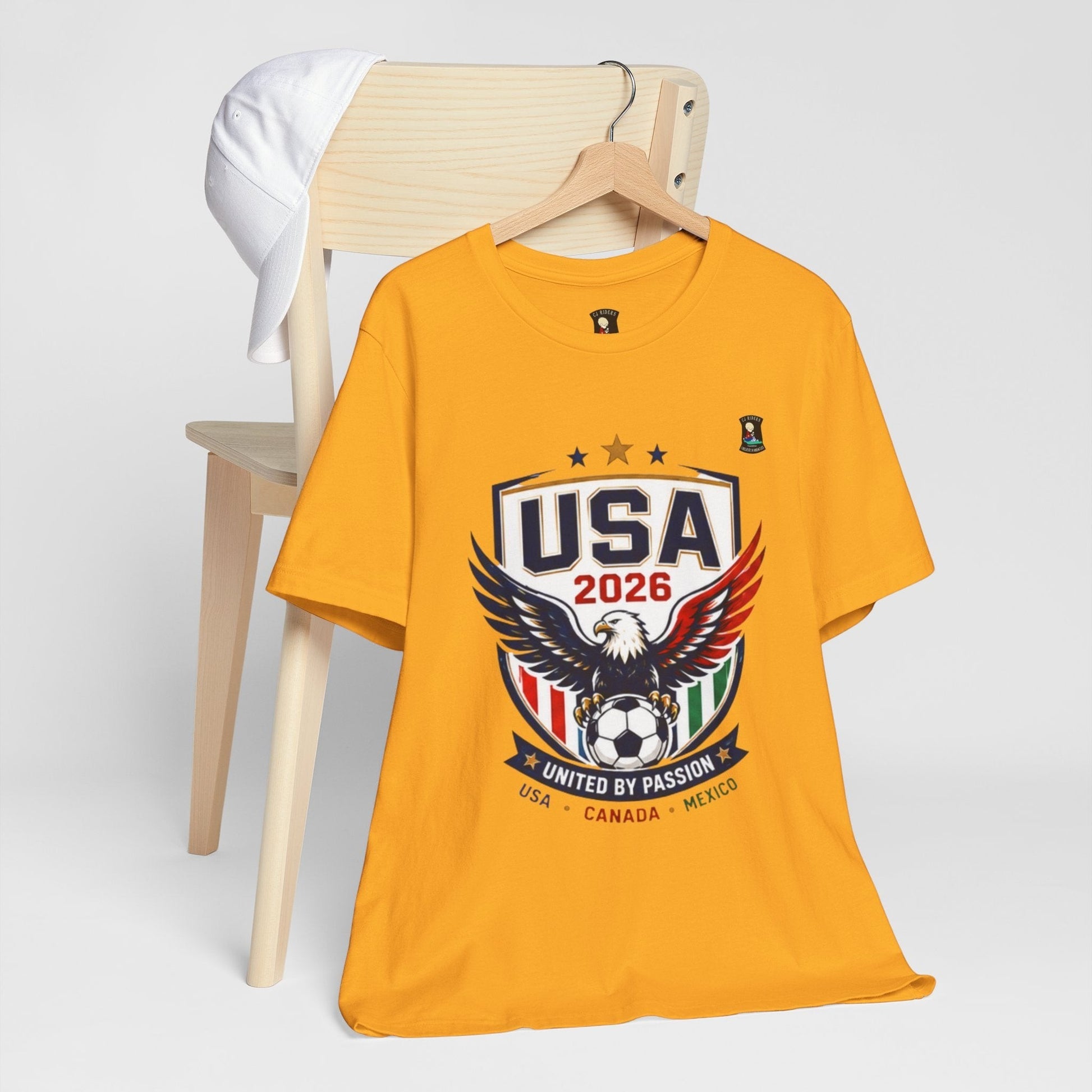 CJ Riders Foundation Store yellow 100% cotton t-shirt with USA 2026 eagle and soccer graphic. Perfect for fans.