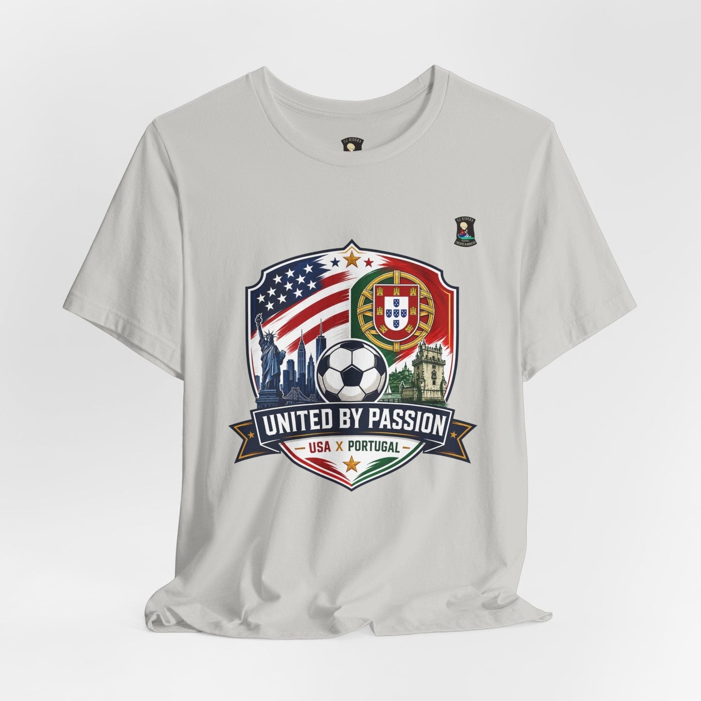 CJ Riders Foundation Store light grey 100% cotton t-shirt with USA & Portugal soccer graphic. Features US flag, Portugal flag, Statue of Liberty, soccer ball, and "United by Passion" text.