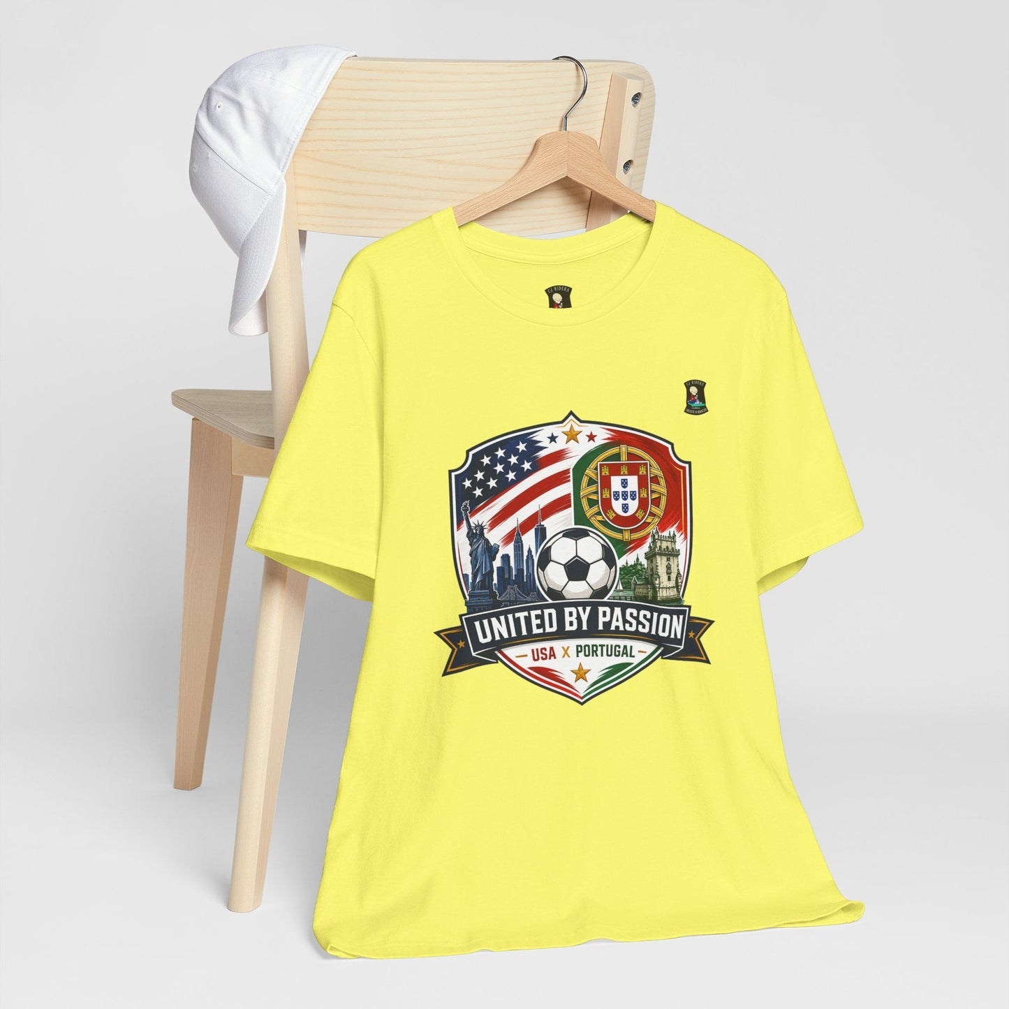 CJ Riders Foundation Store yellow 100% cotton t-shirt with USA & Portugal soccer crest graphic and "United by Passion" text.