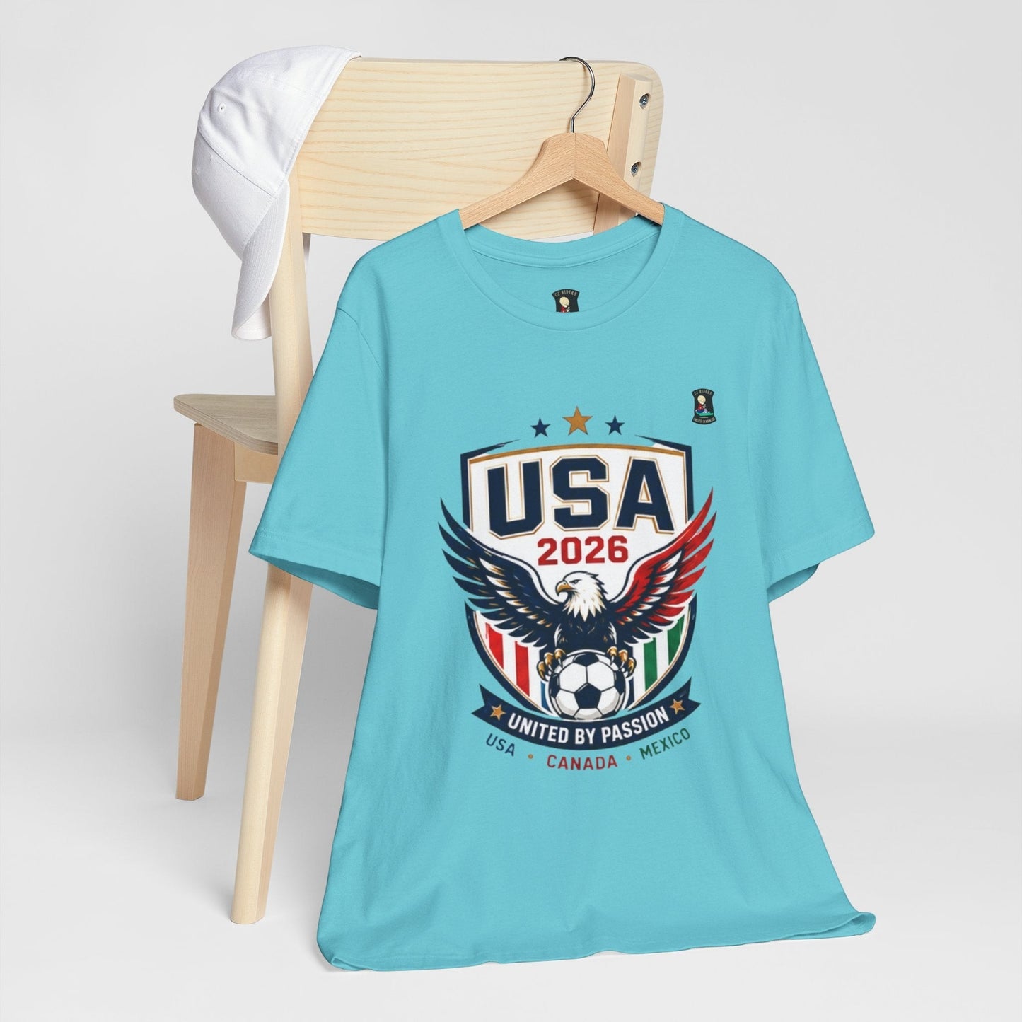 CJ Riders Foundation Store light blue 100% cotton t-shirt with USA 2026 eagle graphic and United by Passion text.