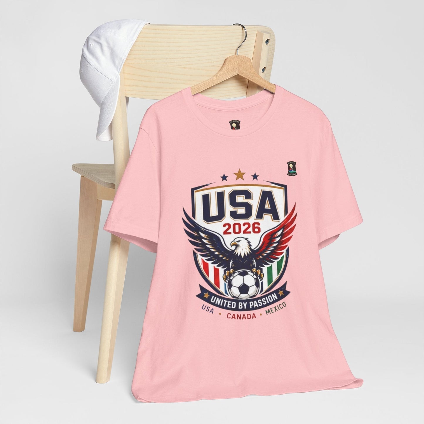 CJ Riders Foundation Store pink 100% cotton t-shirt with USA 2026 eagle and soccer ball graphic. Ideal for soccer fans.
